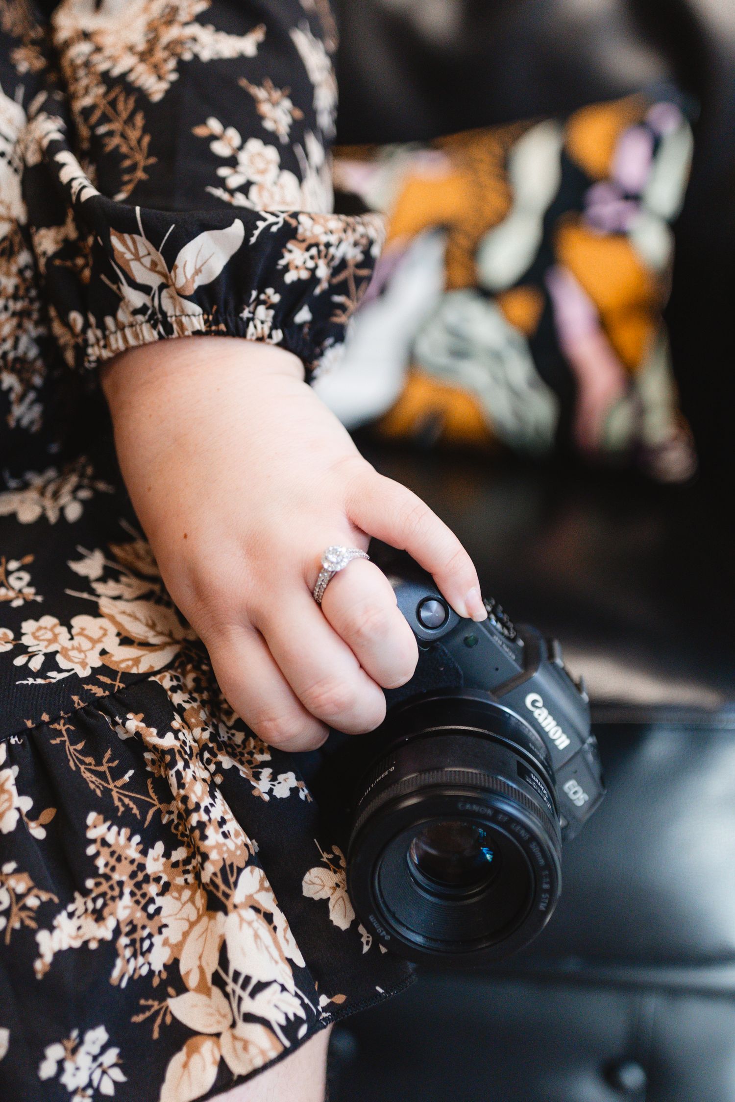 Close-up of hands holding professional camera while wearing floral print dress.