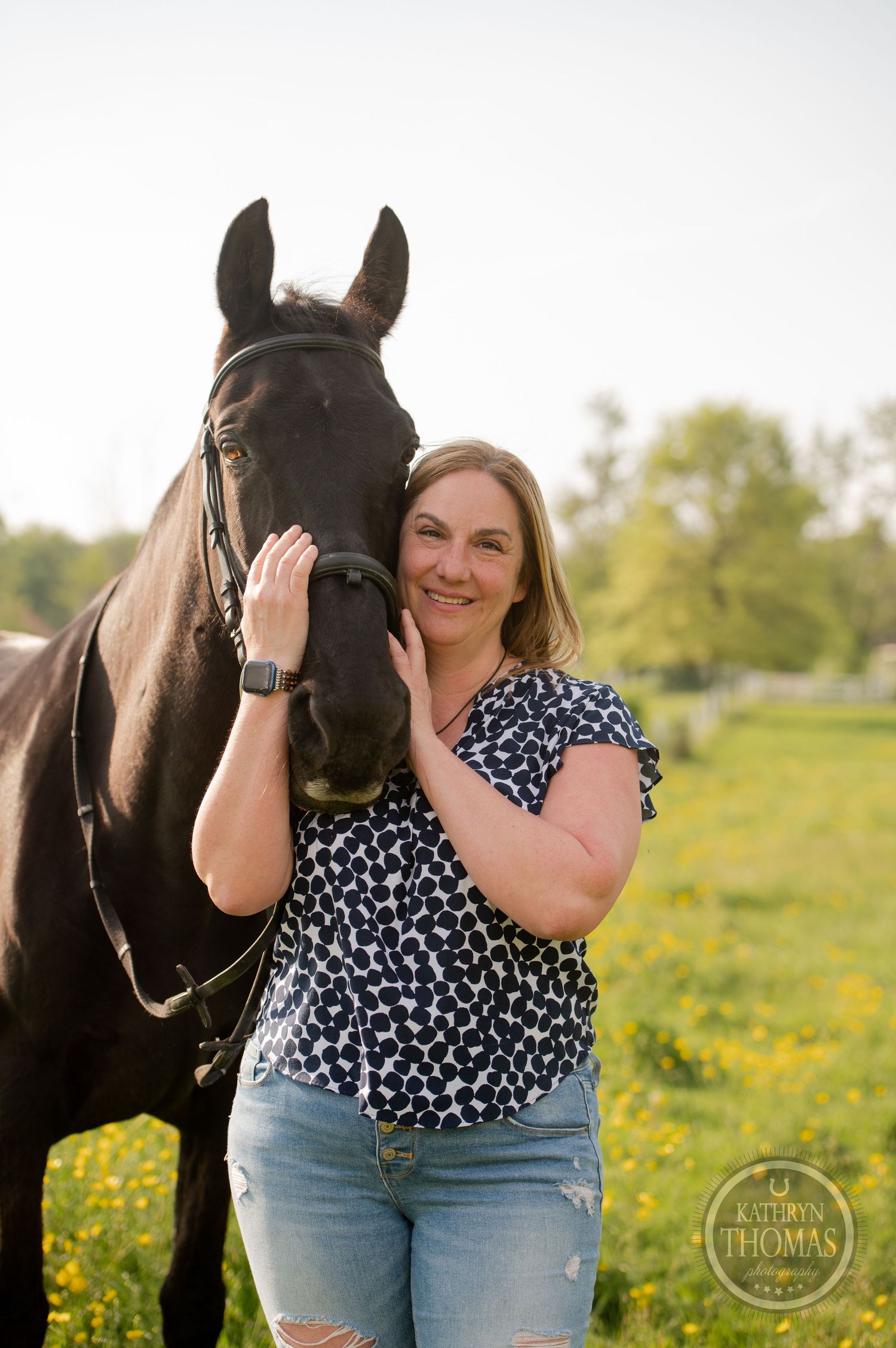 A close-up of a black horse and person in a flowery spring field.