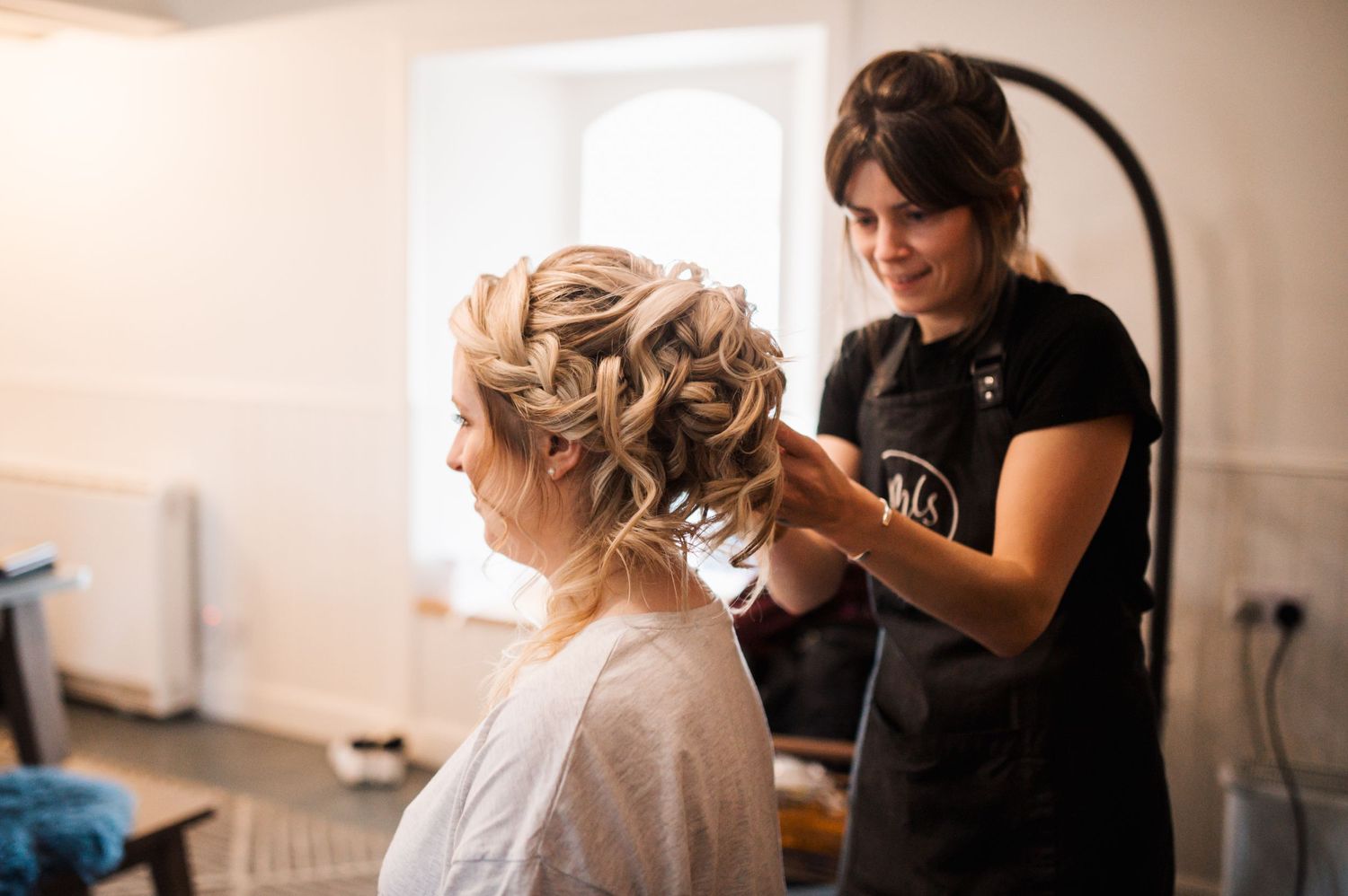 Hair stylist works on an elegant updo hairstyle in a bright salon setting.