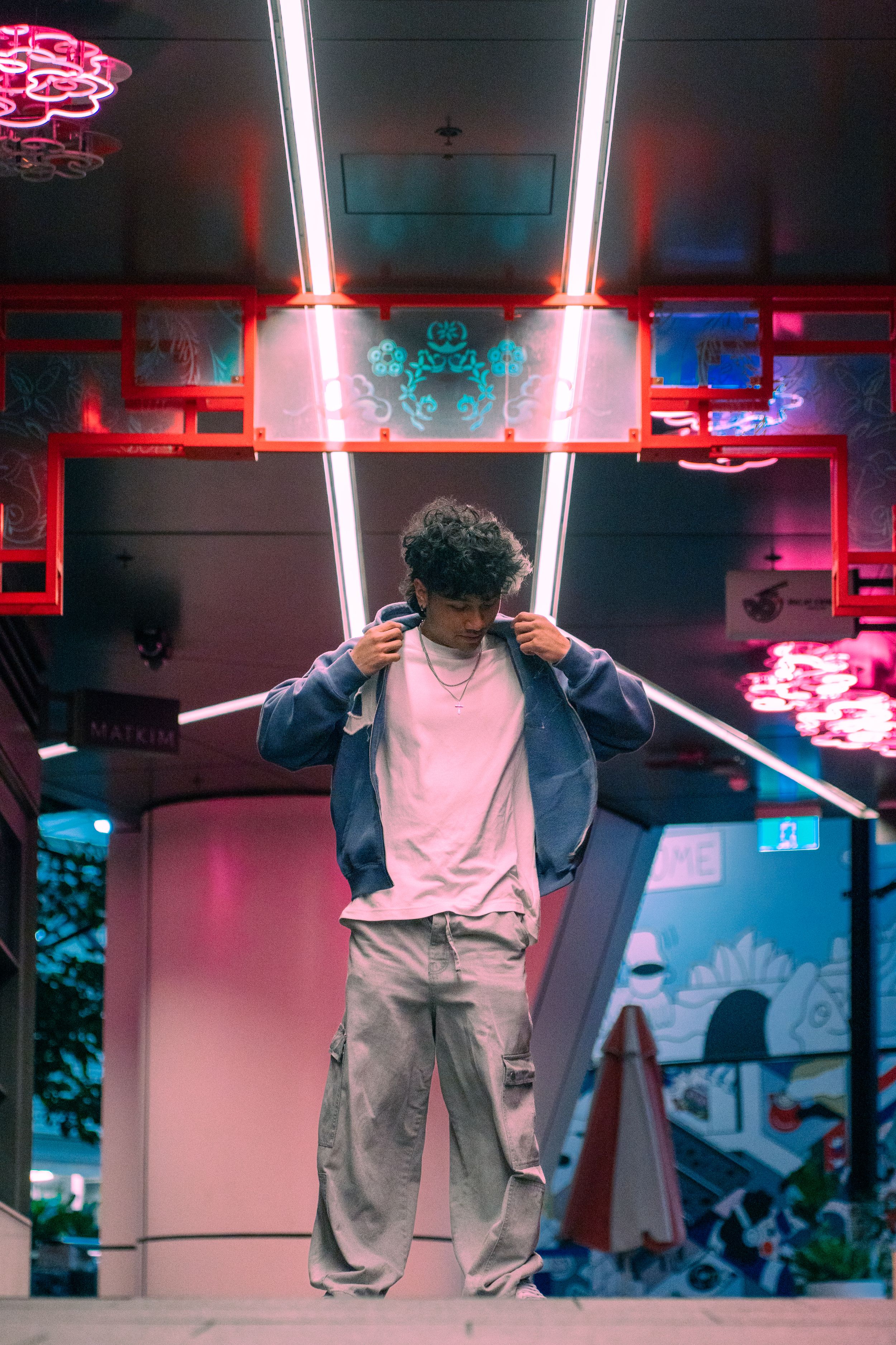 Young man adjusting jacket under vibrant neon lights at night venue.