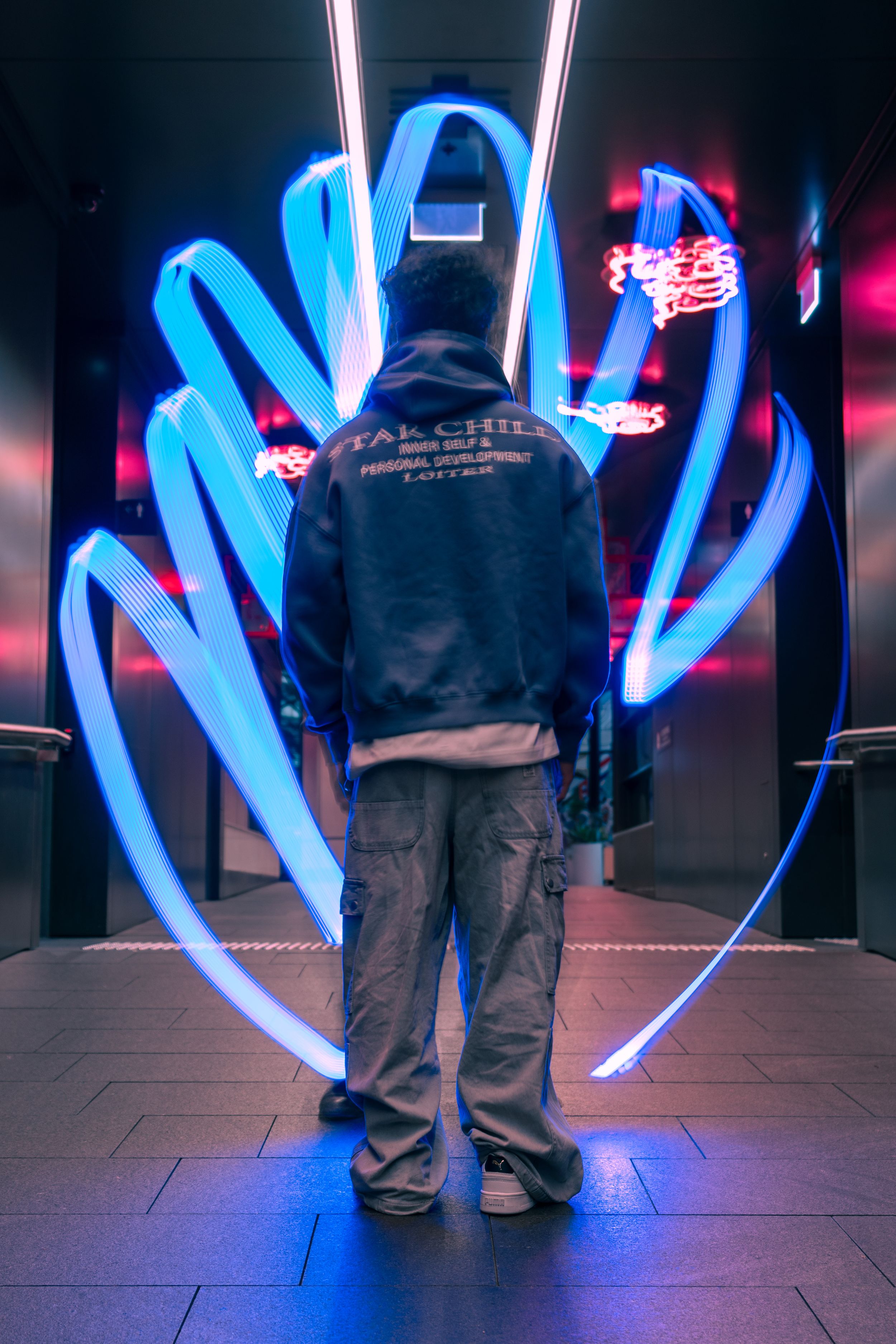 Person in hoodie standing before glowing blue neon light art installation.