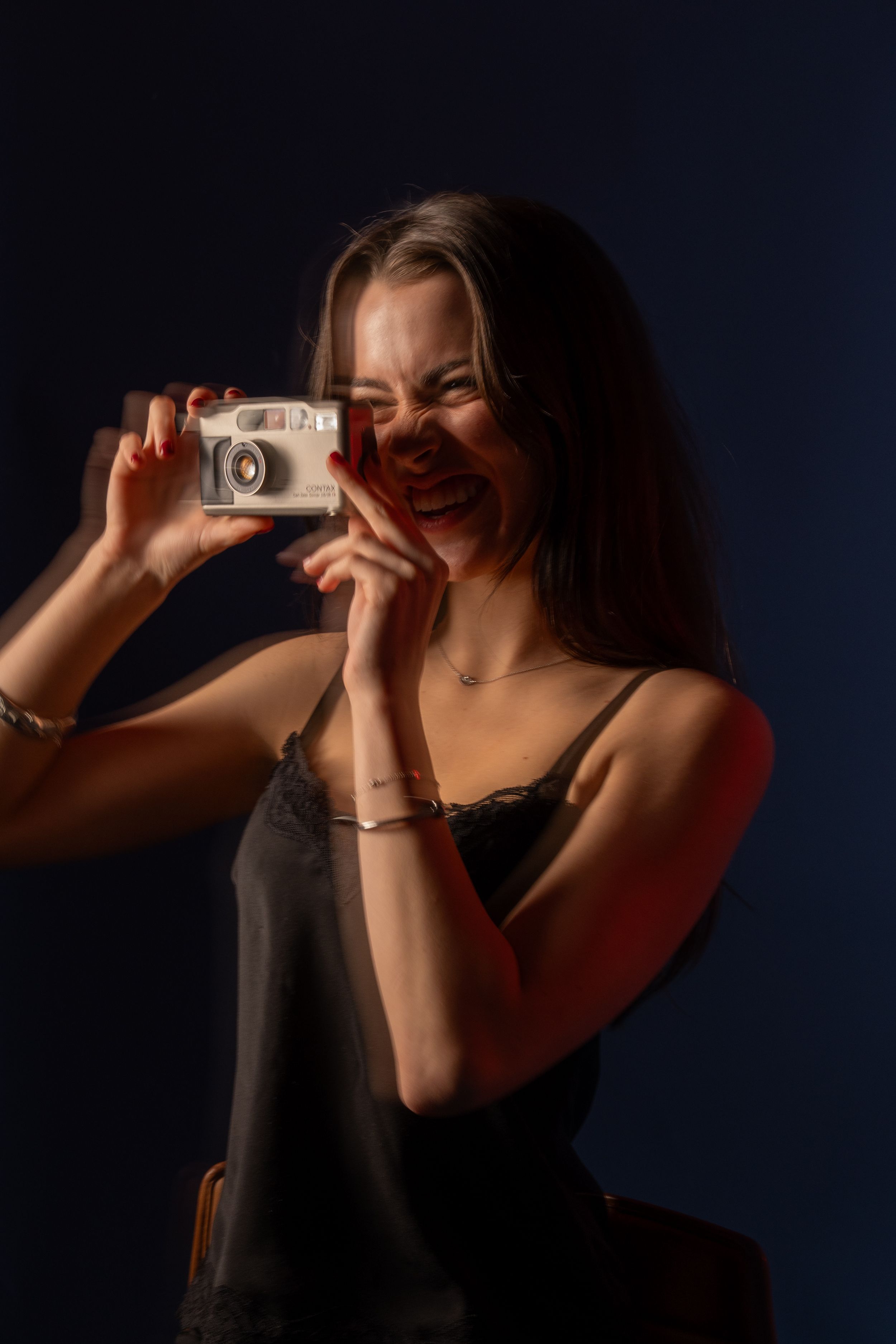 Laughing young woman holding a vintage film camera in a dark studio with red light.