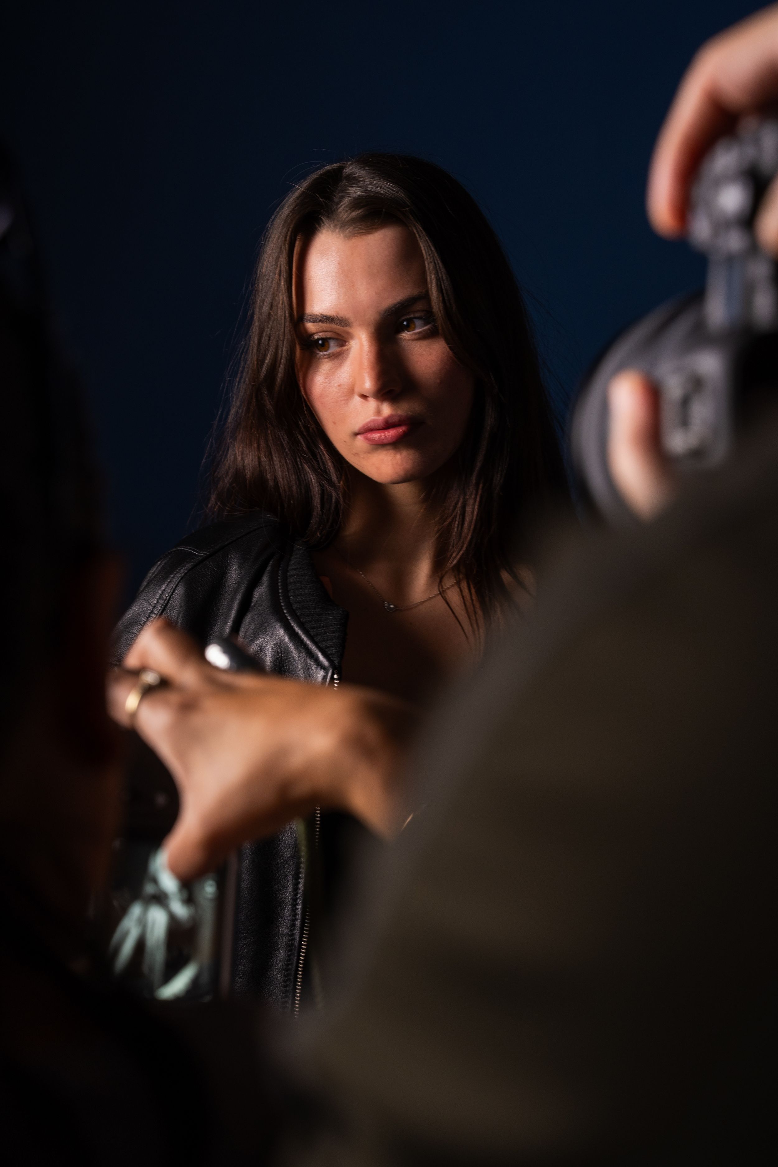 Brunette woman in leather jacket photographed in moody dark blue studio setting.