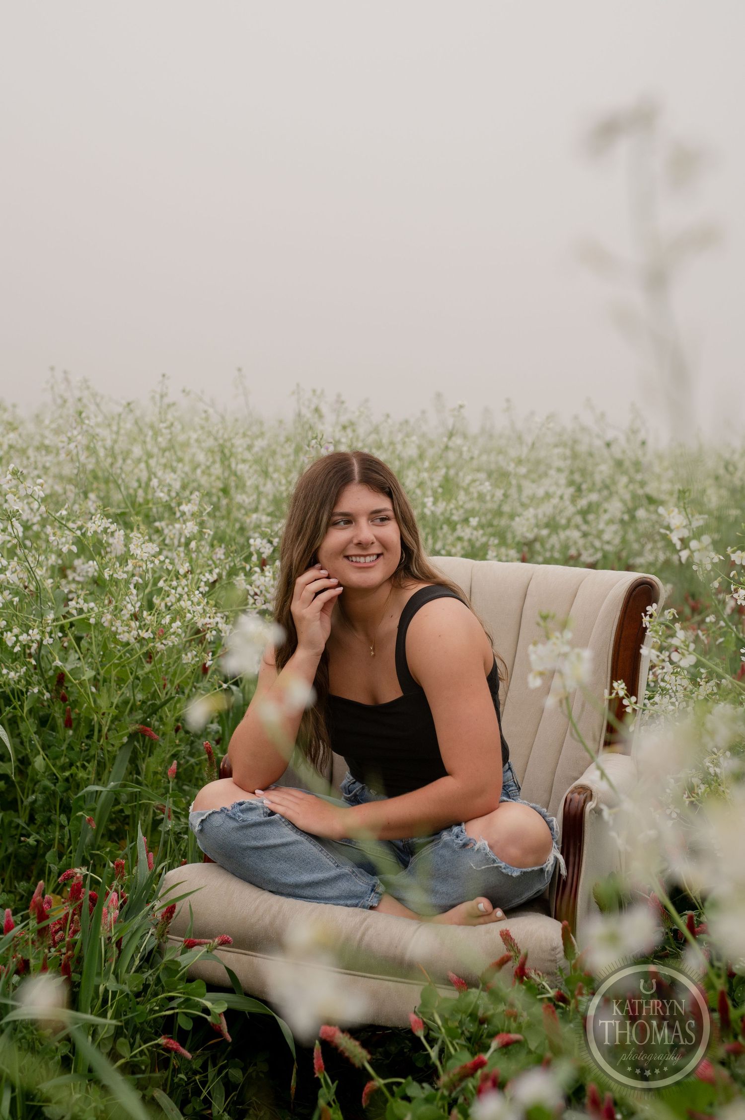 A joyful outdoor portrait amid white wildflowers with a vintage beige armchair as prop.