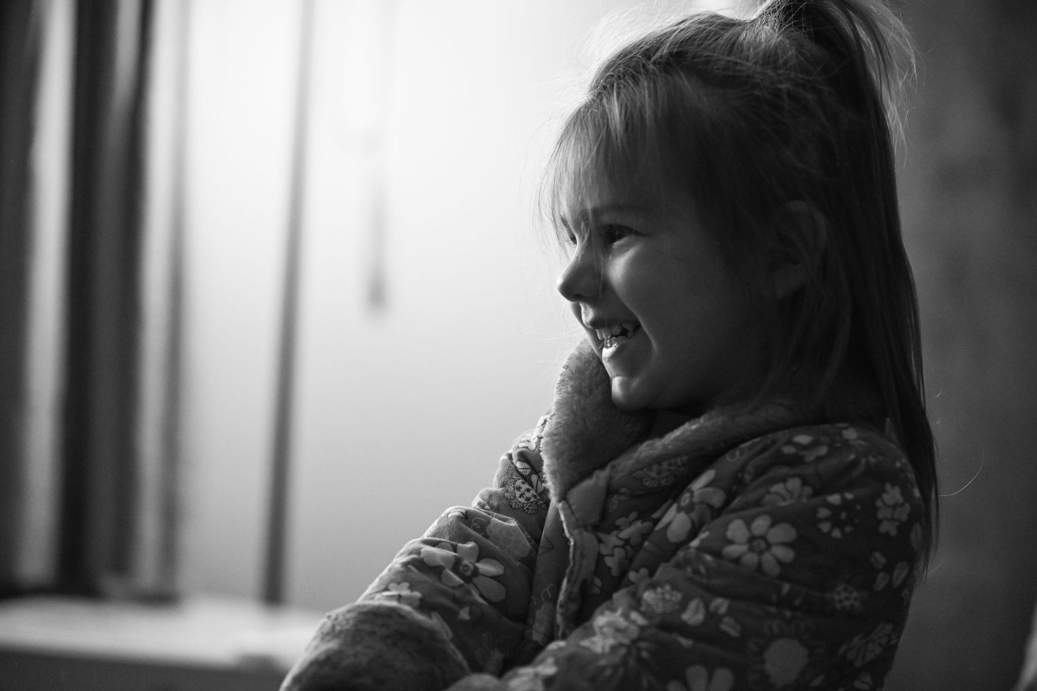 A black and white photograph of Emma, a little girl, smiling in her coat