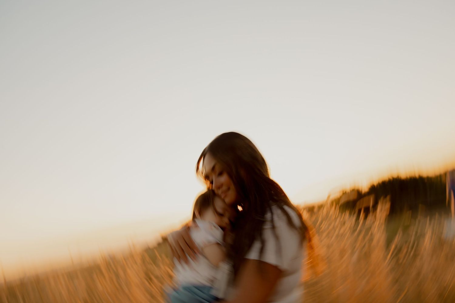 Silhouette of mother and child embracing during sunset in a field.