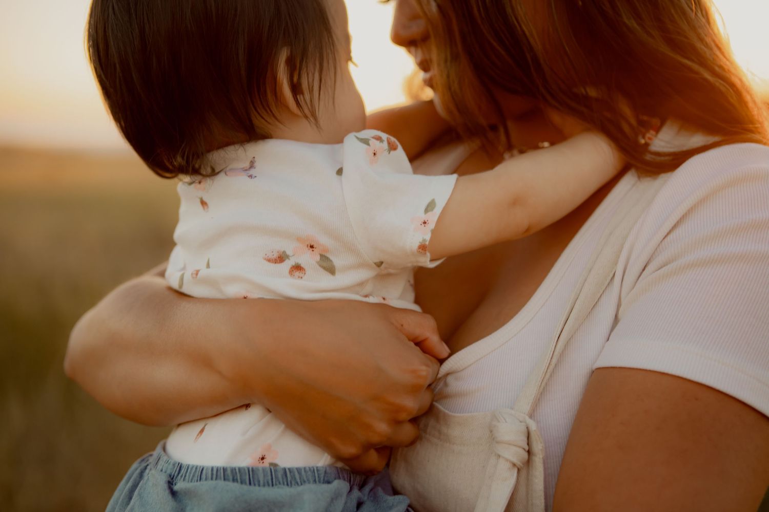 Close-up of mother holding baby against golden sunset backdrop.
