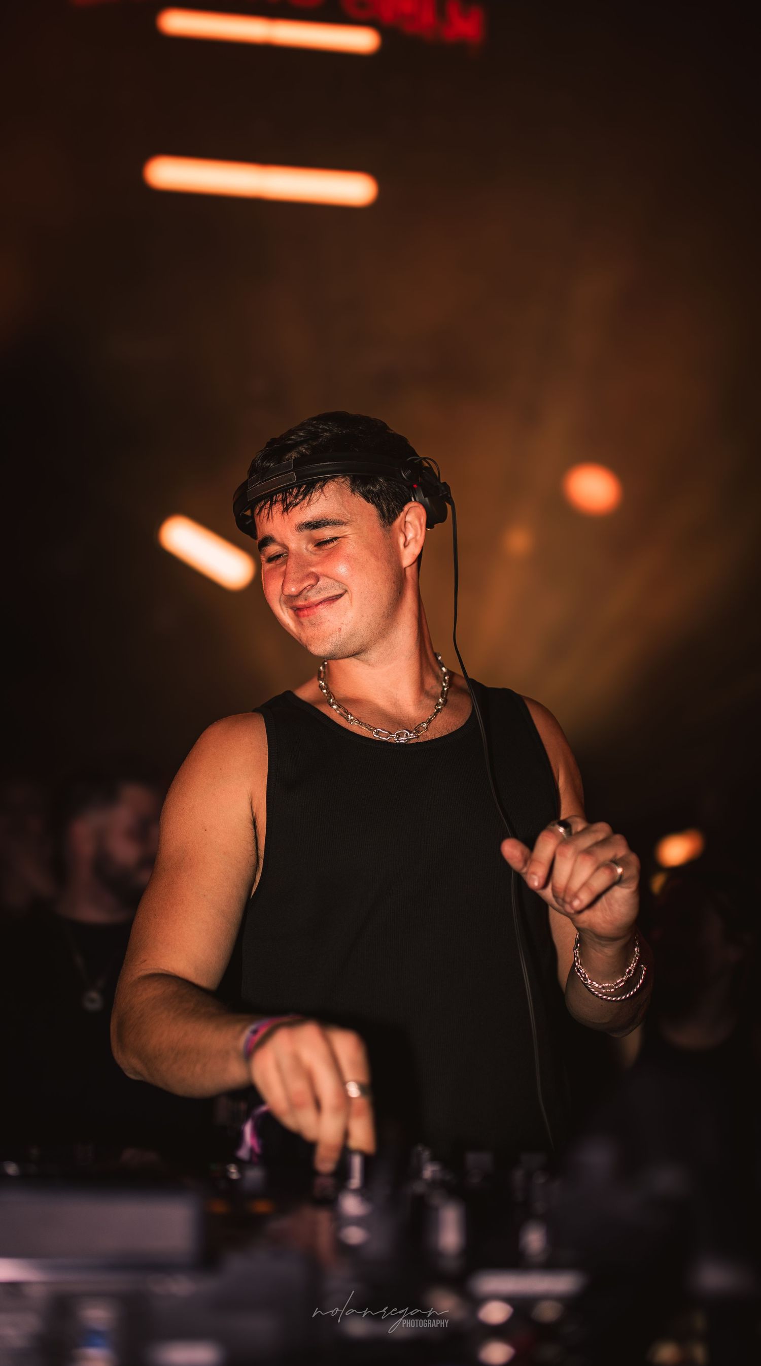 DJ performing at a nightclub with orange lighting and dark atmosphere.