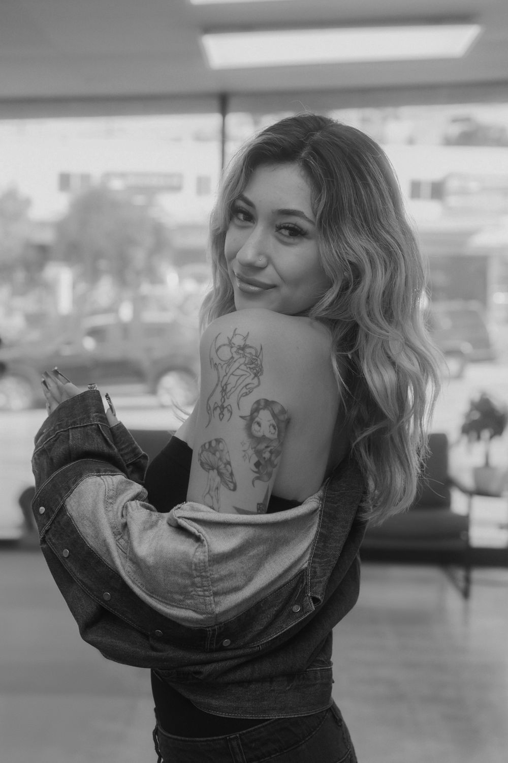 Black and white portrait showcasing tattoo art on shoulder in a salon setting.