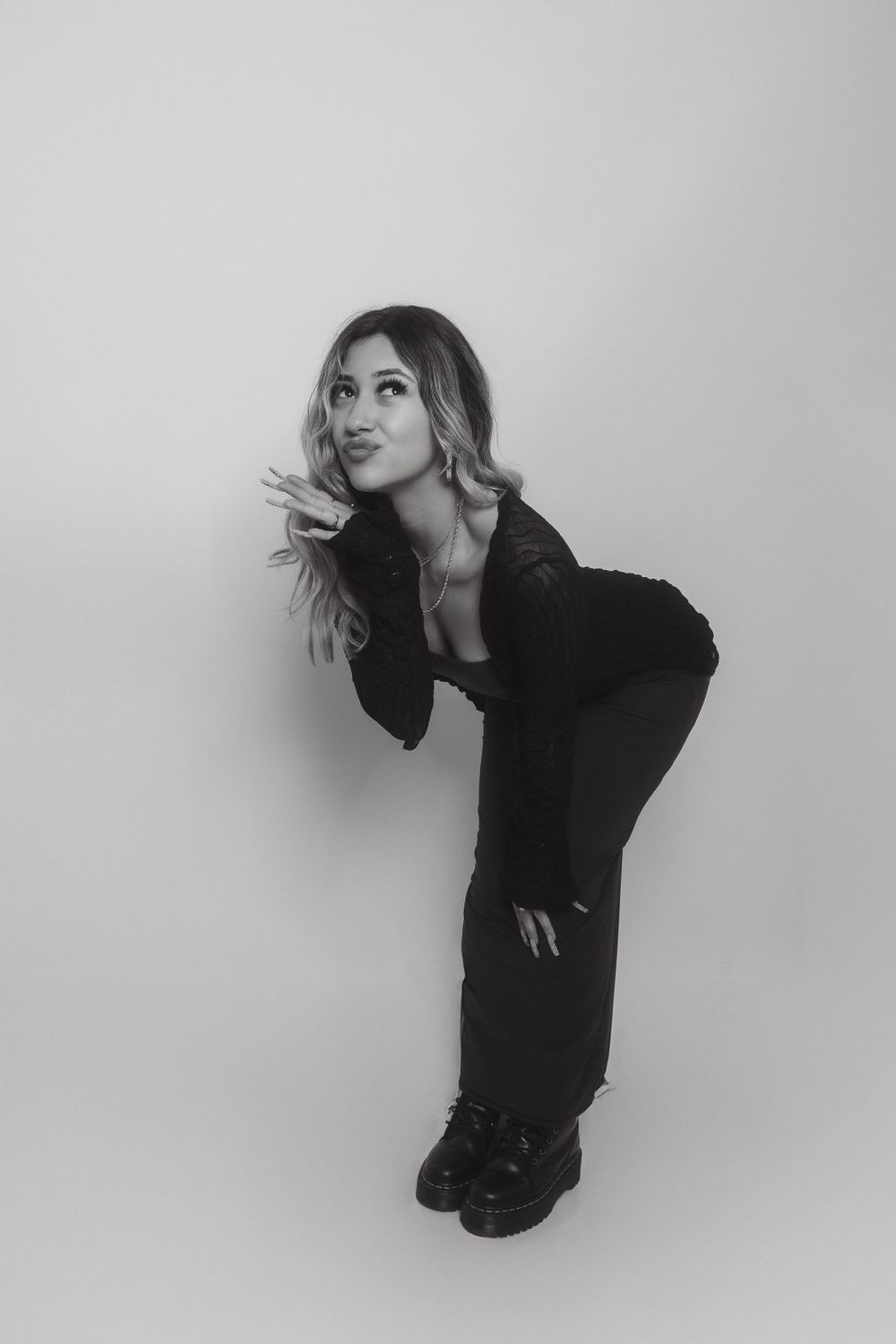 Artistic fashion pose in all black outfit against minimalist grey backdrop.