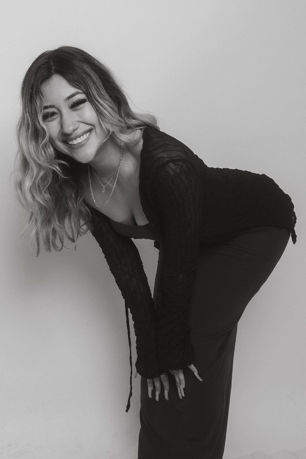 Stylish portrait showing blonde wavy hair and black outfit against grey background.
