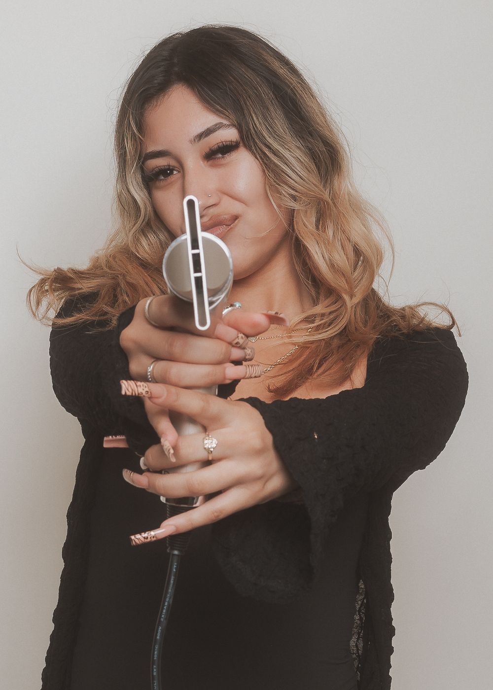 Hairstylist holding hair cutting tools against grey backdrop in artistic portrait.