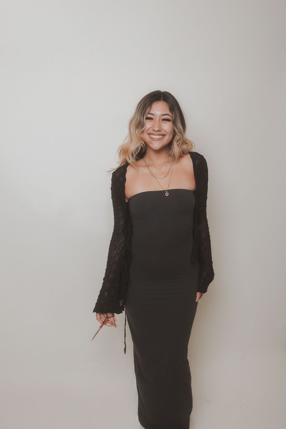 Stylish portrait in a black dress and cardigan against a neutral background.