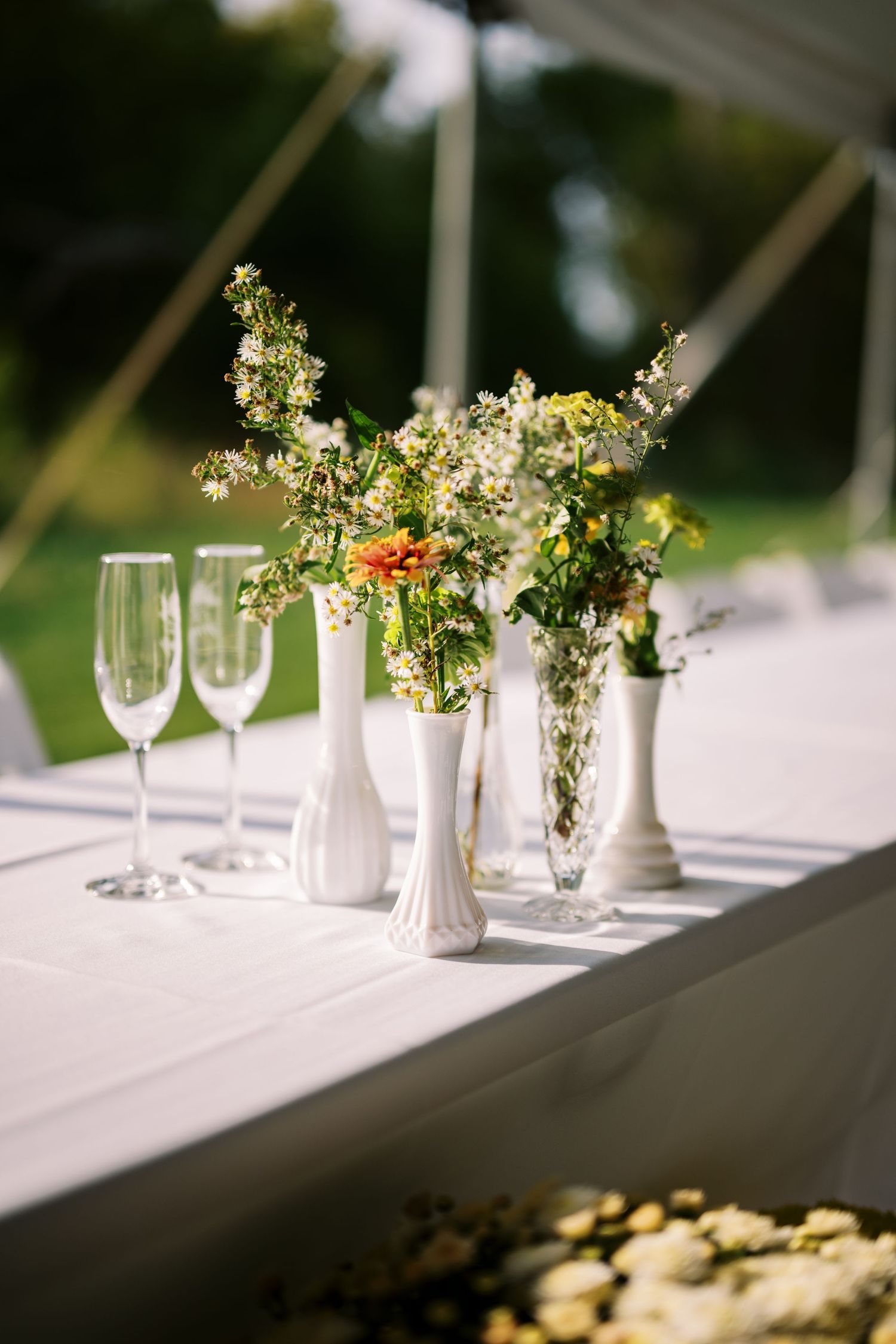 Elegant table setting with white vases of wildflowers and champagne glasses on a crisp white tablecloth.