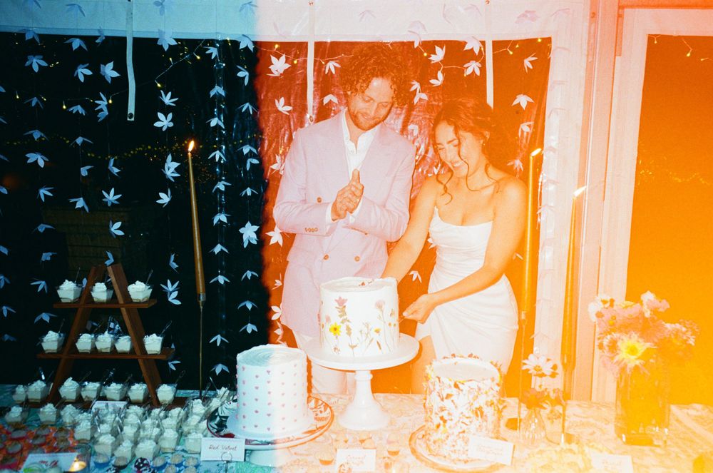 Couple cutting wedding cake at reception with star backdrop and colorful light leak effect.