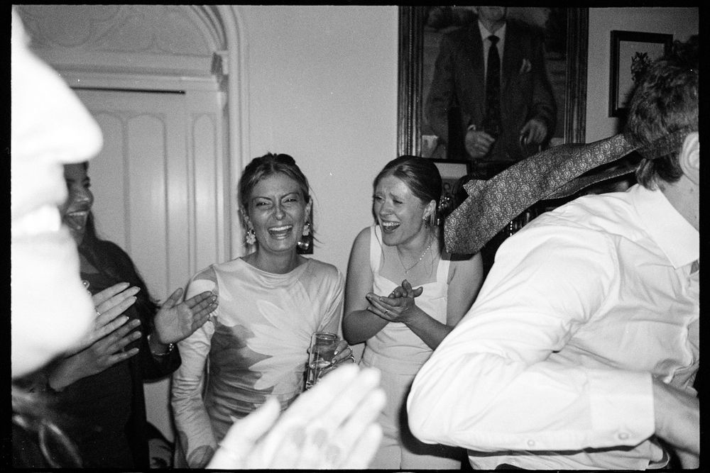 Black and white photo of joyful wedding guests laughing and celebrating during the reception.