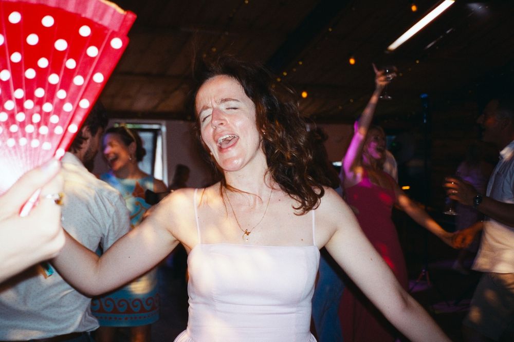 Woman in white dress dancing joyfully at a lively party, holding a red polka dot fan.