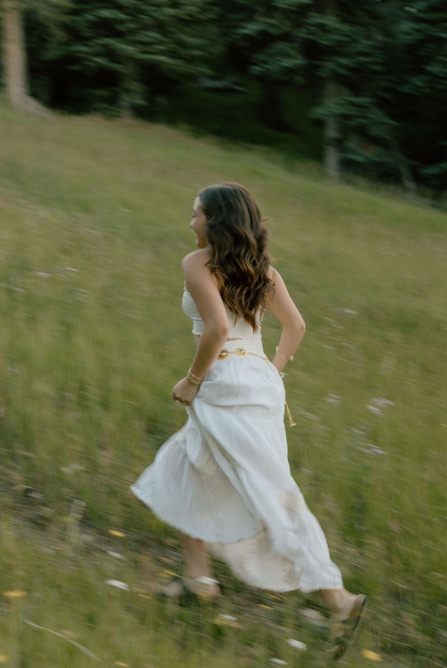 A cinematic photo of a girl in a flowing white dress twirls gracefully through a sunlit meadow with tall grass and trees in the background.