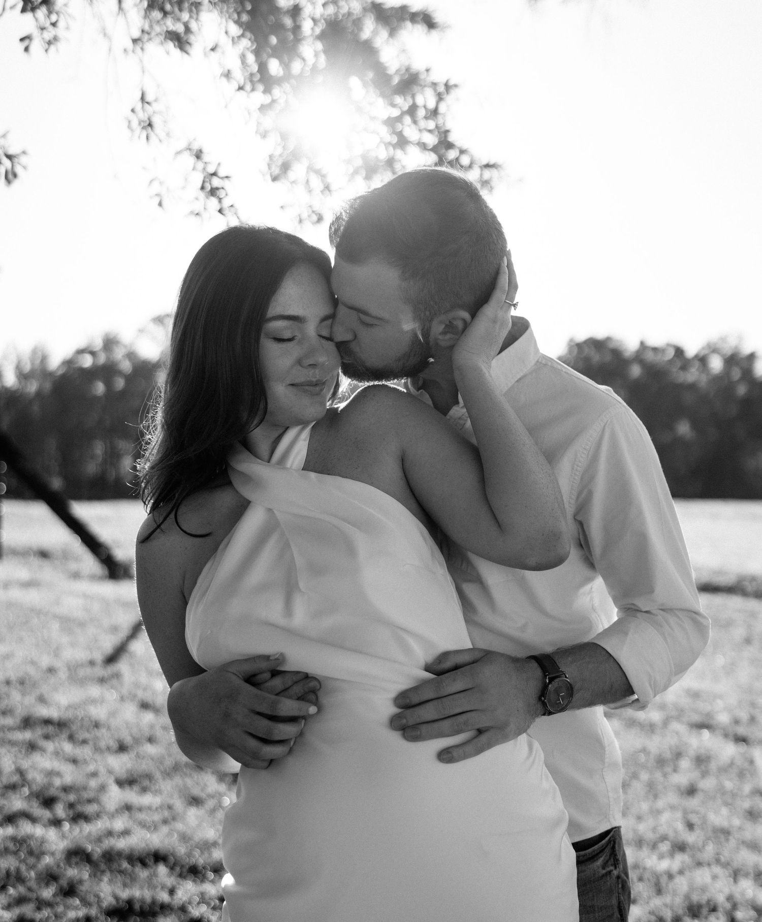 A couple embraces tenderly in a sunlit outdoor setting, captured in a series of romantic black and white photographs.
