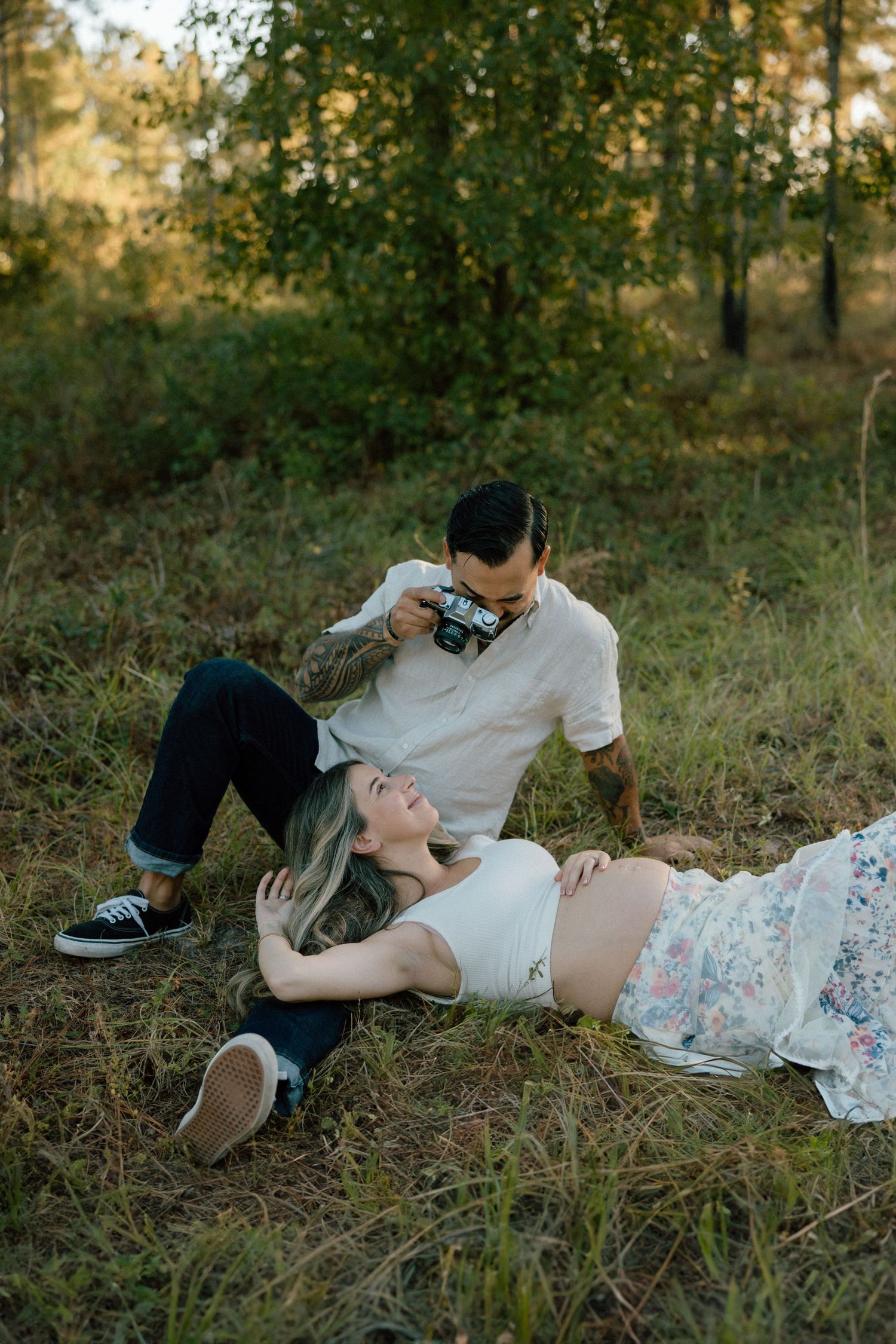 A cinematic photo of a couple relaxes together in a grassy field  during golden hour, with trees and sunlight in the background.
