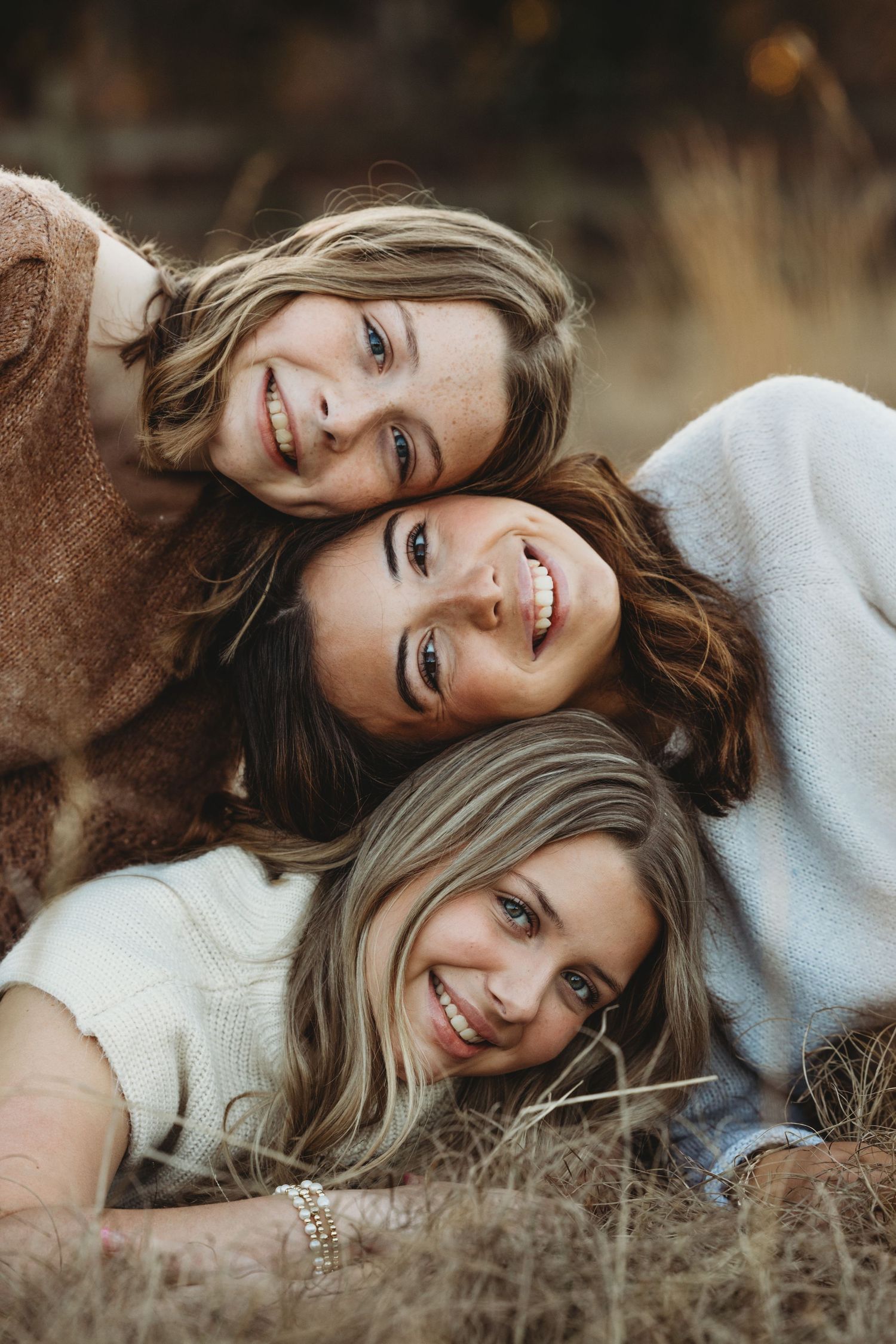 Three friends laying together in tall grass during golden hour.
