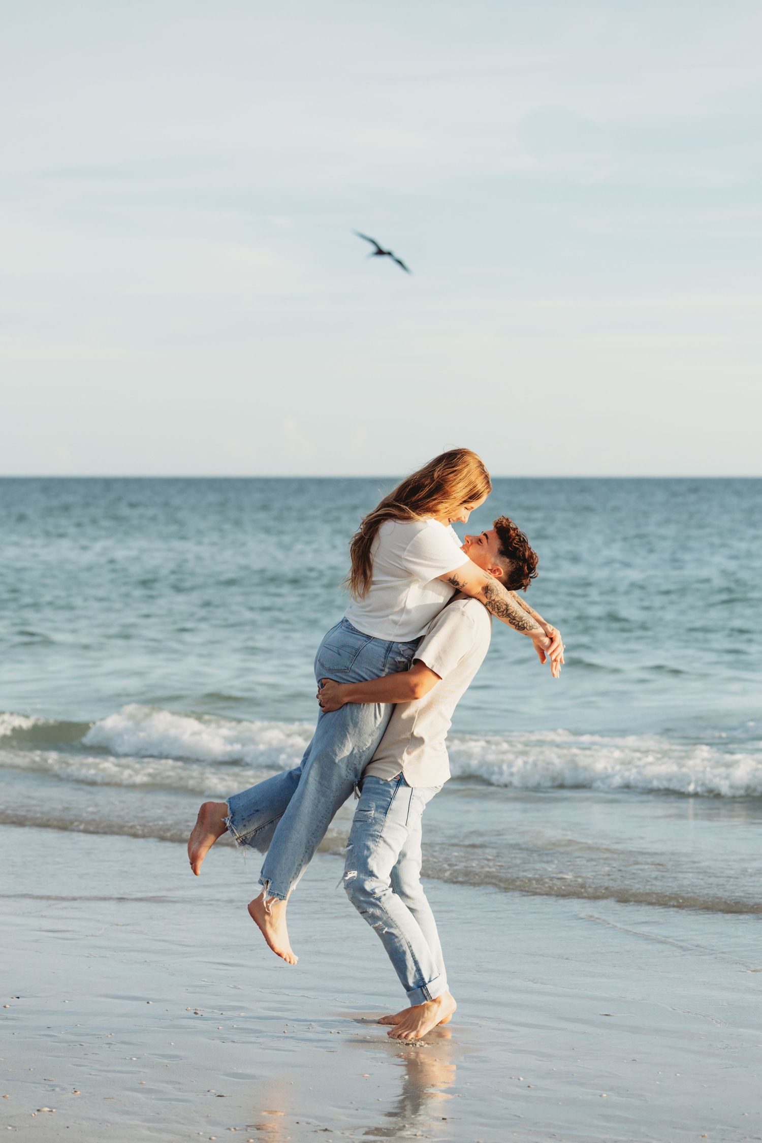 A romantic moment on the beach as a couple embraces with a seagull flying overhead.
