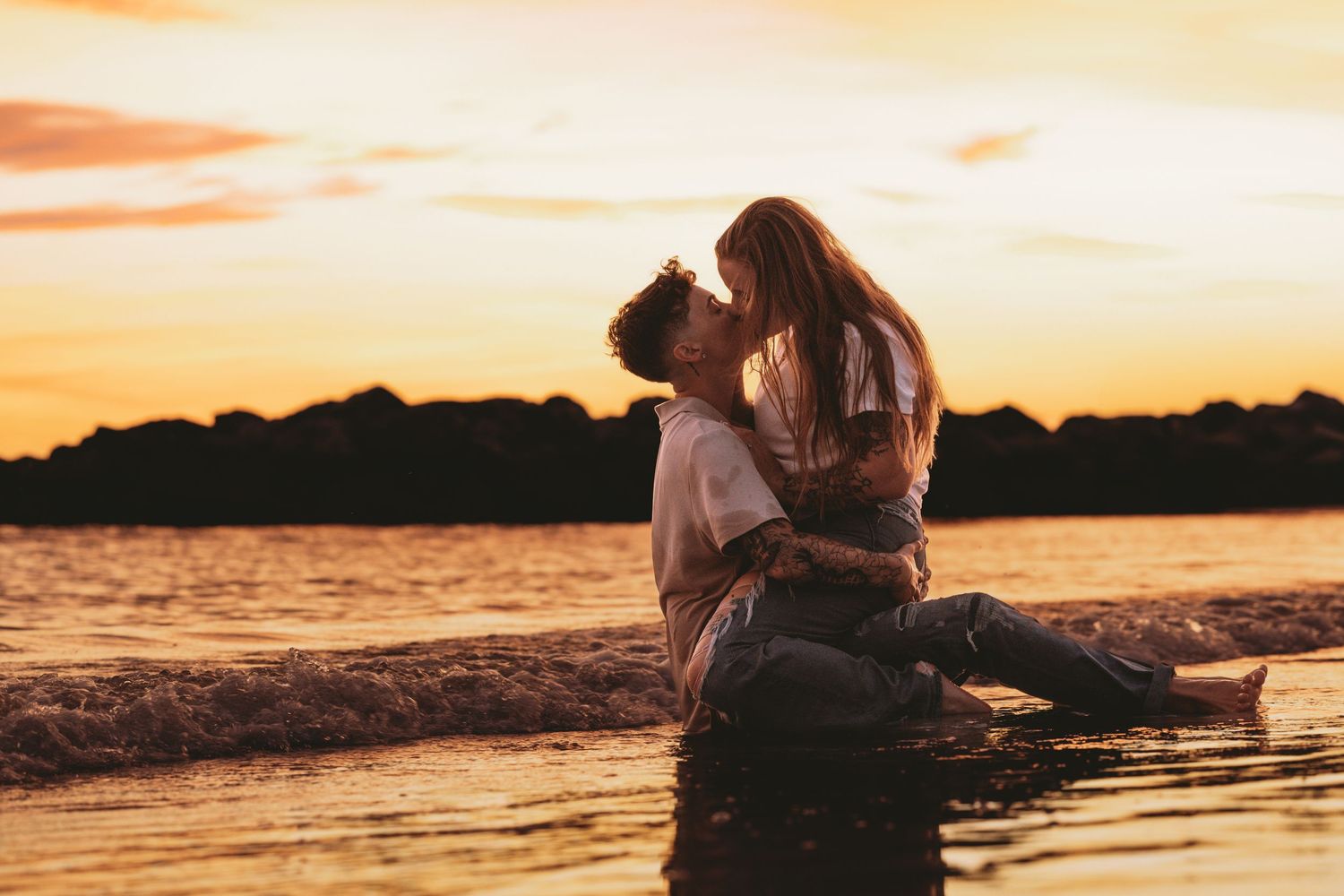 A couple sharing an intimate moment by the water during a golden sunset.