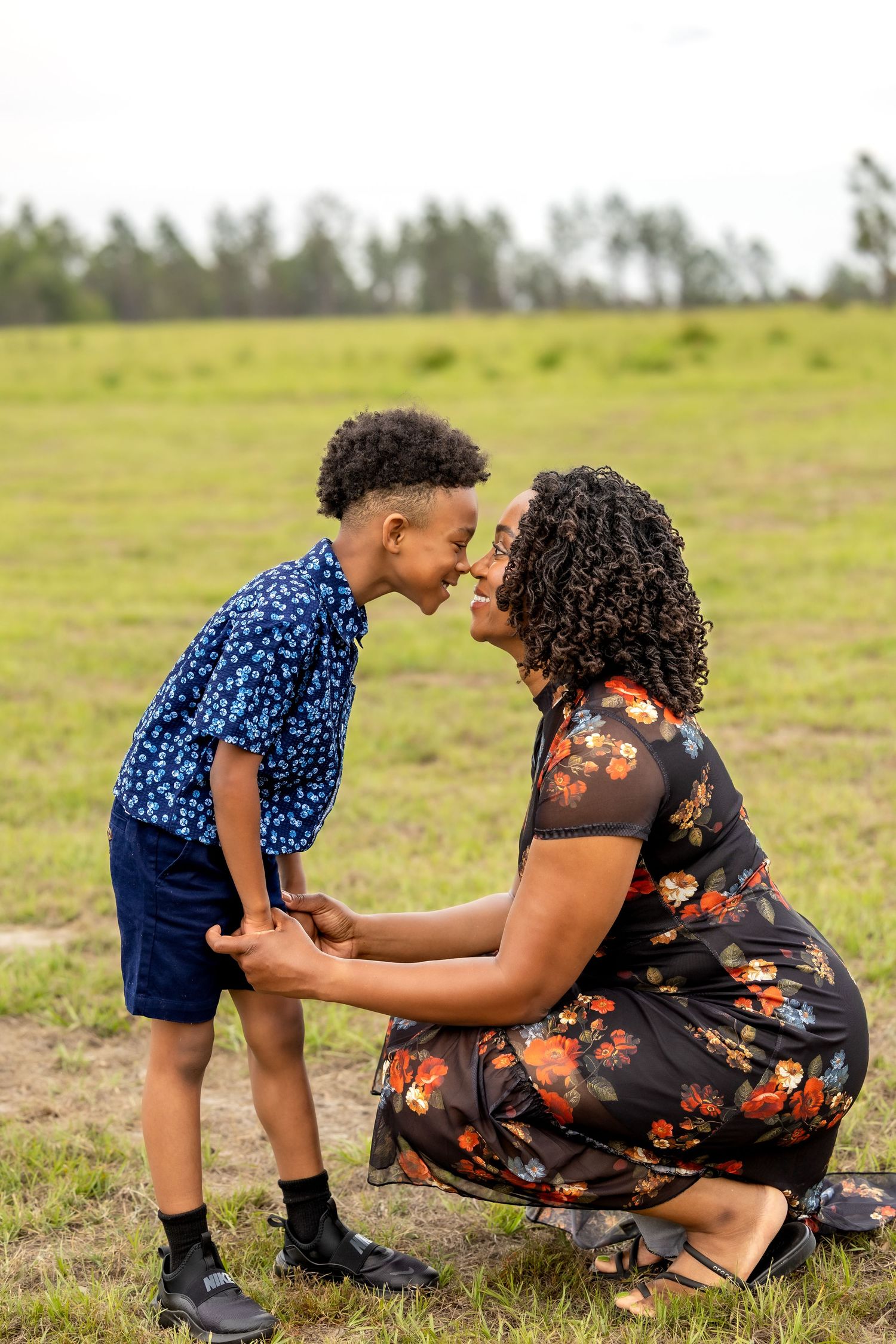A mother and young son share a tender nose-to-nose moment outdoors in a green field.