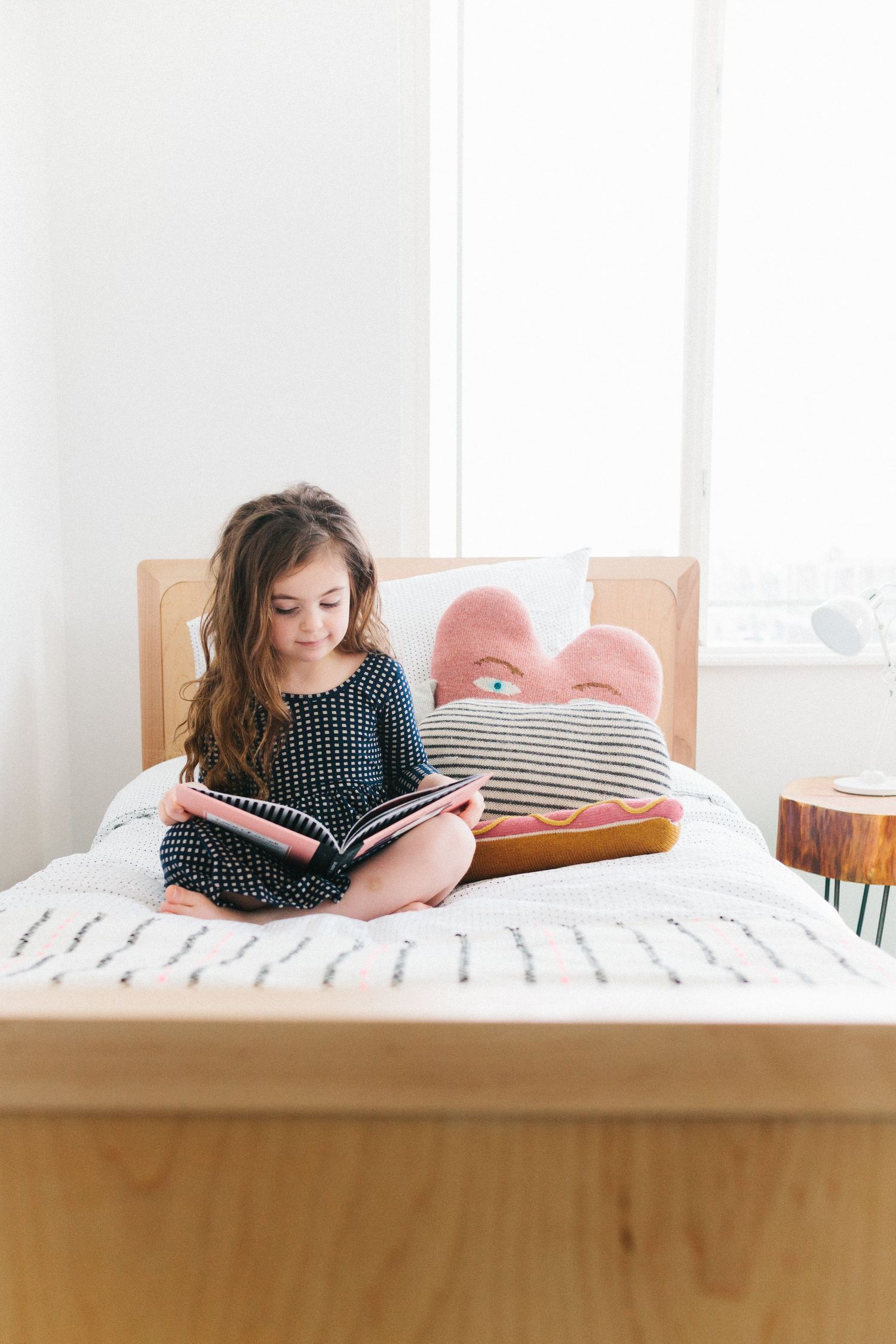 a  little girl sitting cross legged on a bed reading a book