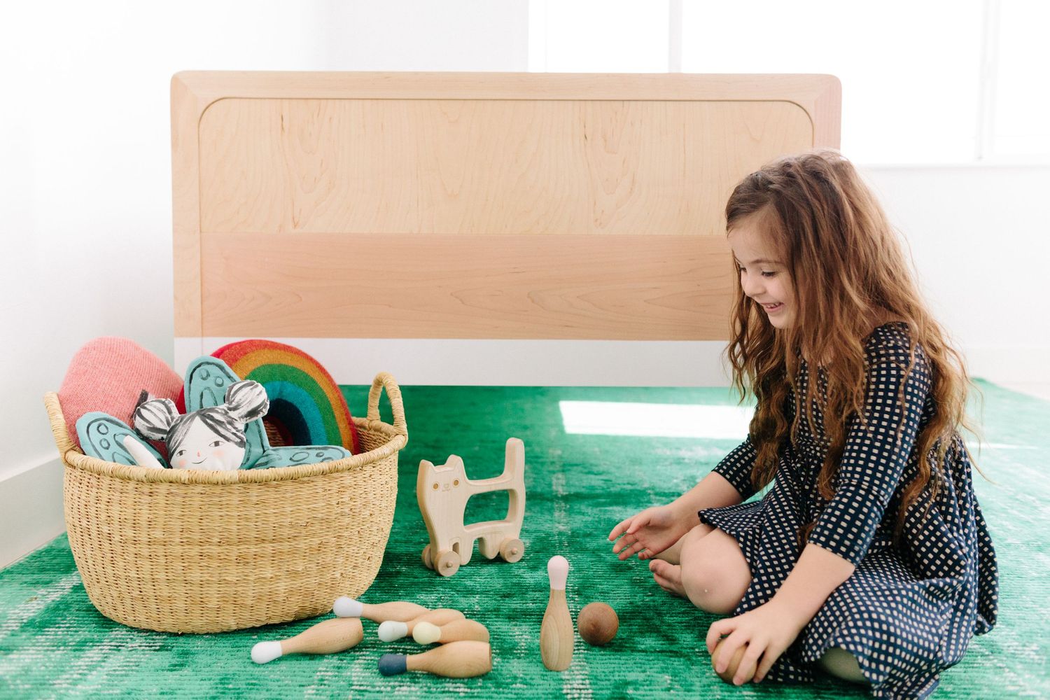 little girl sitting on the ground playing with a basket of toys and wooden bowling pins