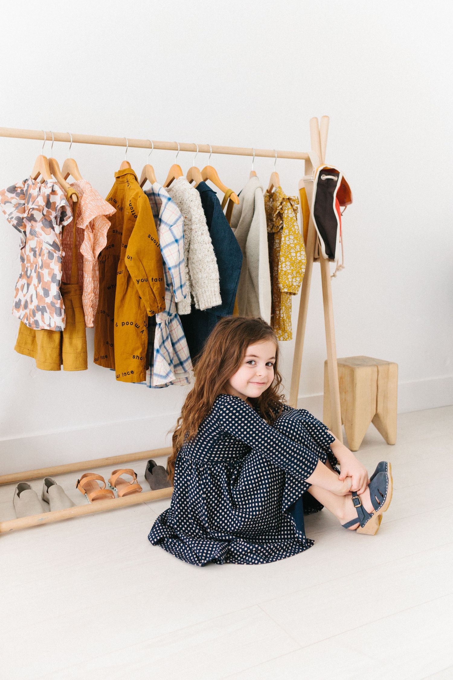 little girl sitting in a dress in front of a clothes rack