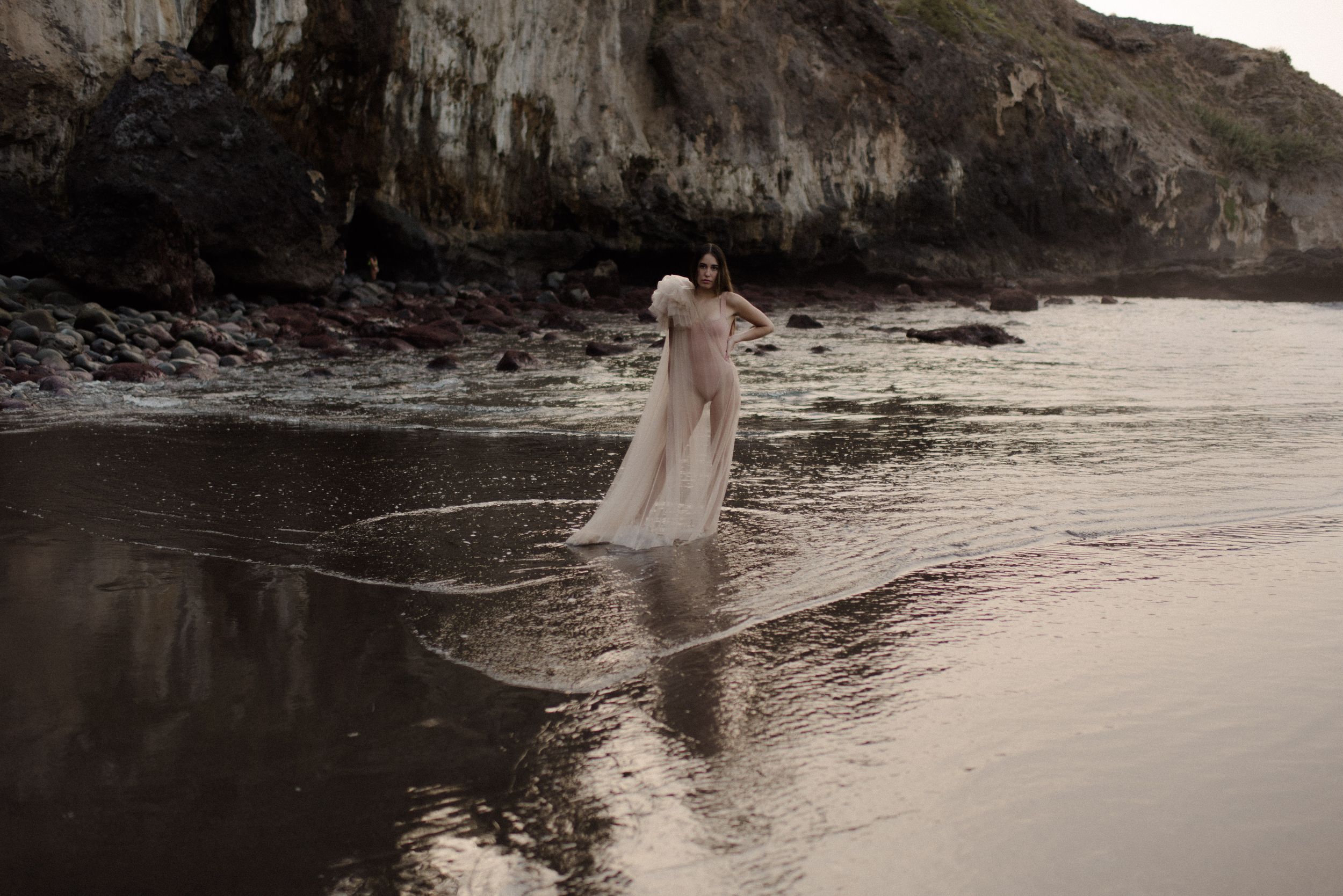 Artistic silhouette of a figure in flowing fabric against dramatic coastal cliffs at sunset.