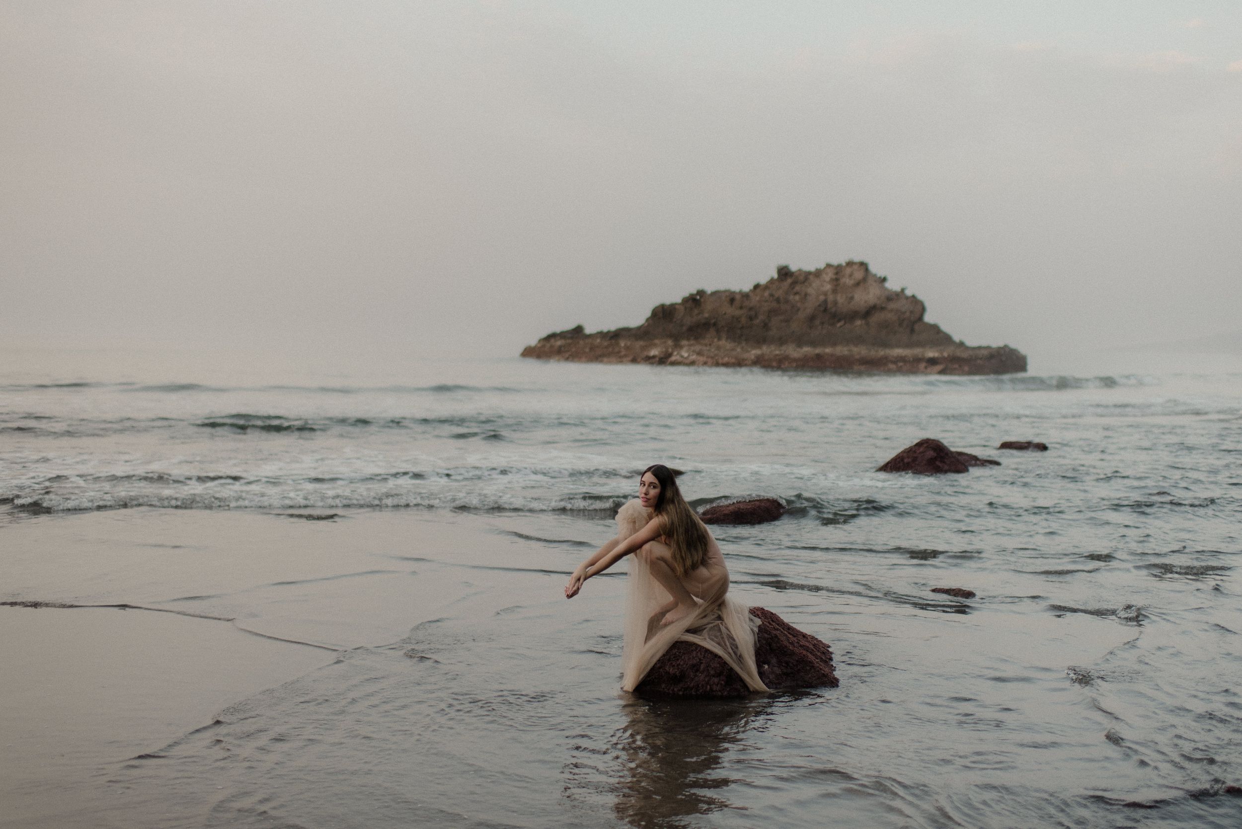 A scenic beach landscape with waves crashing against rocky outcrops during sunset.