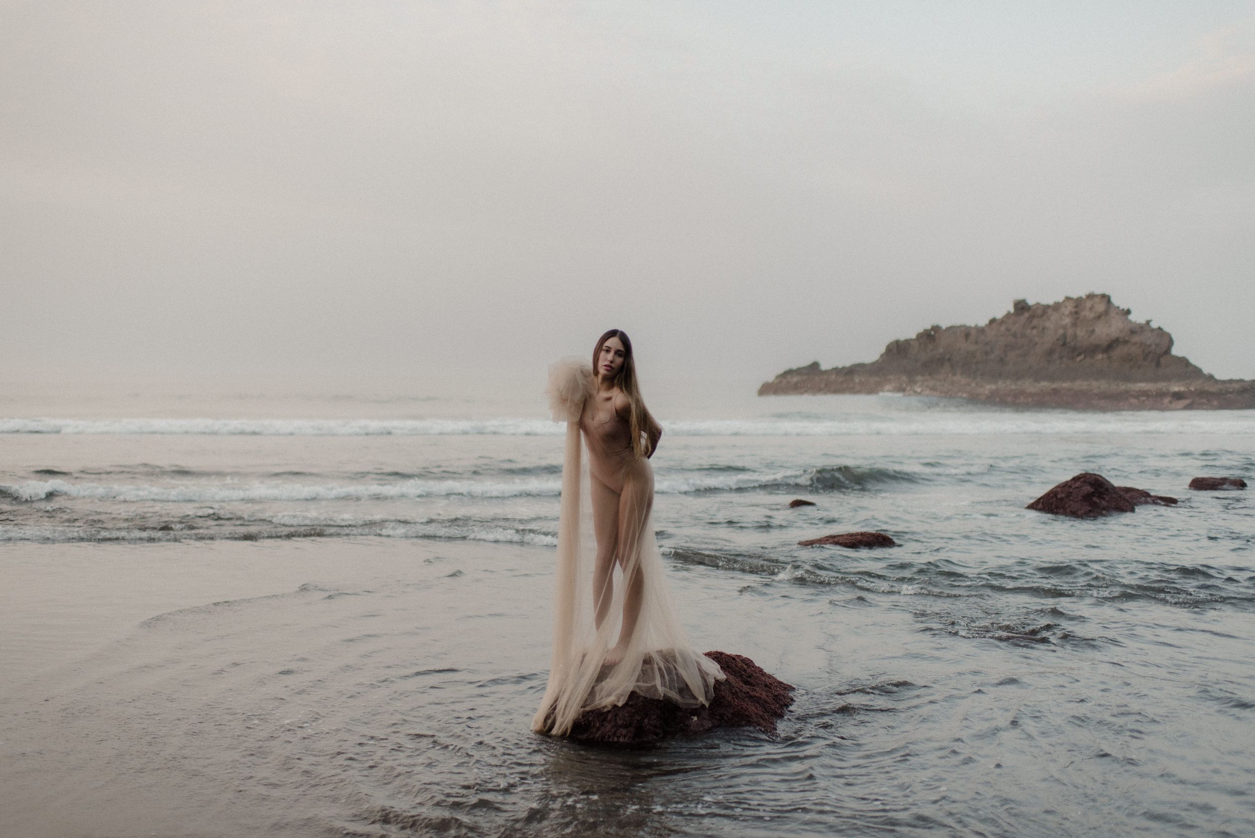 Ethereal beach scene with figure in light fabric walking along misty shoreline.