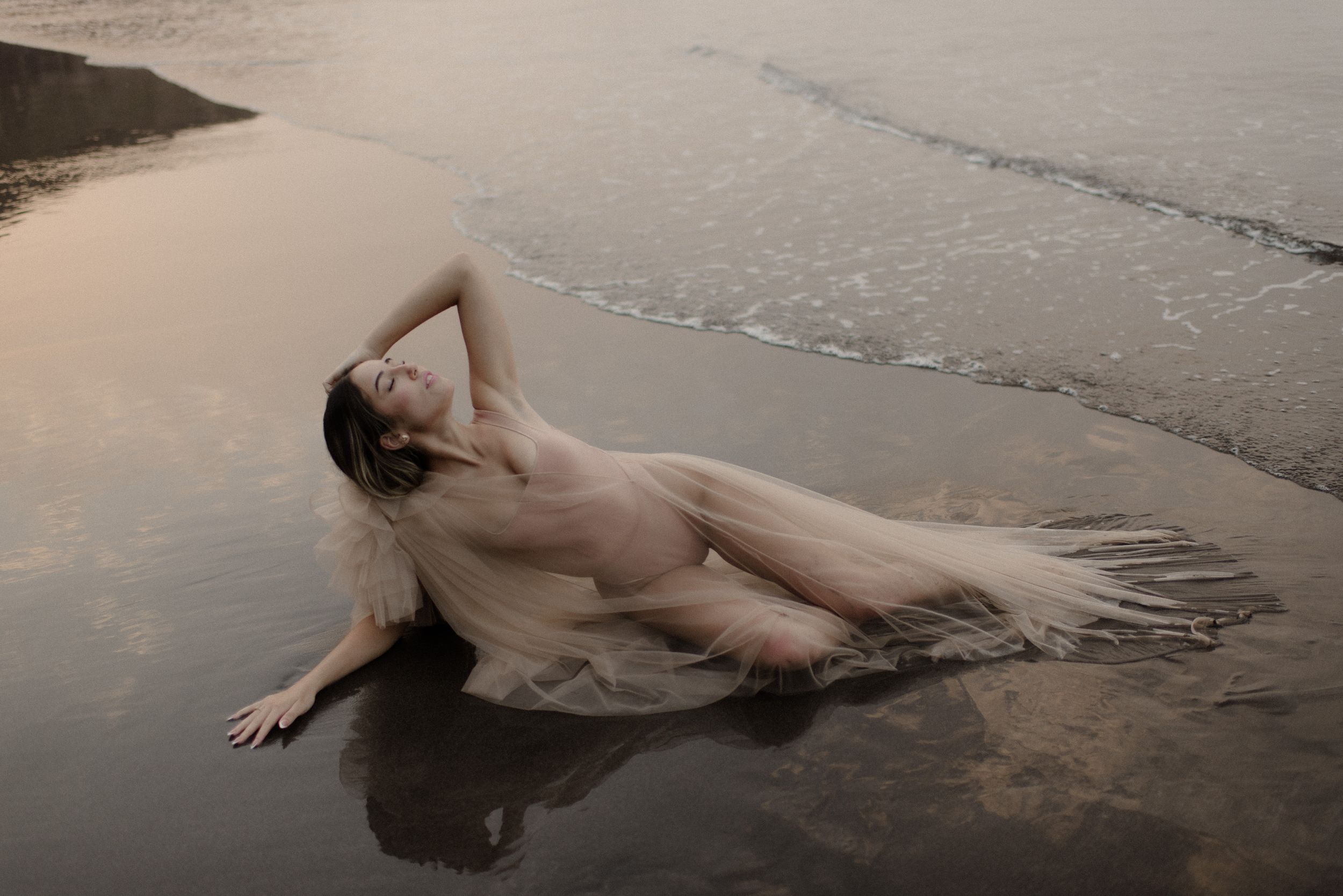 Minimalist coastal photography with figure reclining on wet sand at water's edge.