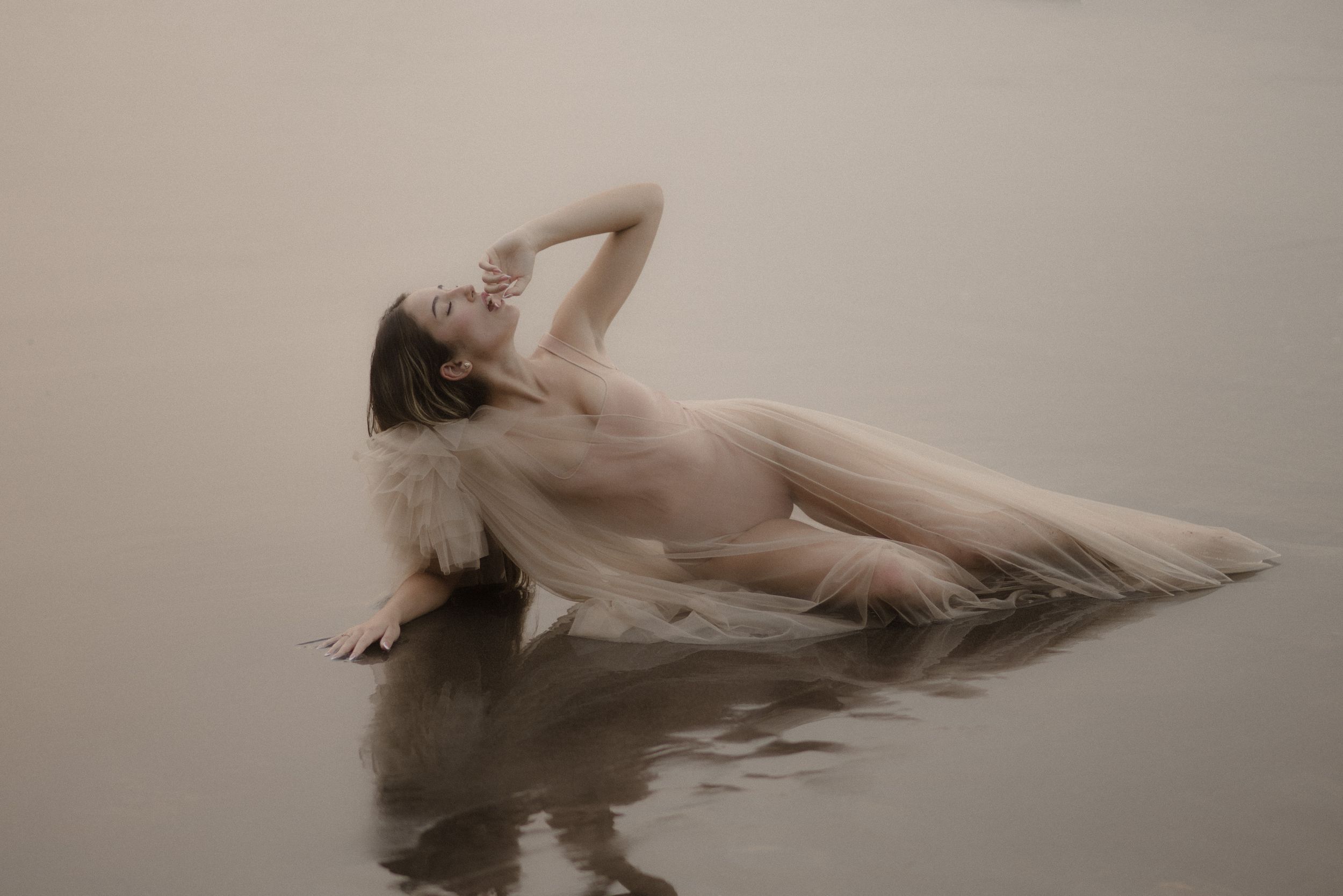 An ethereal beach scene with a flowing white dress creating artistic movement in the sand.