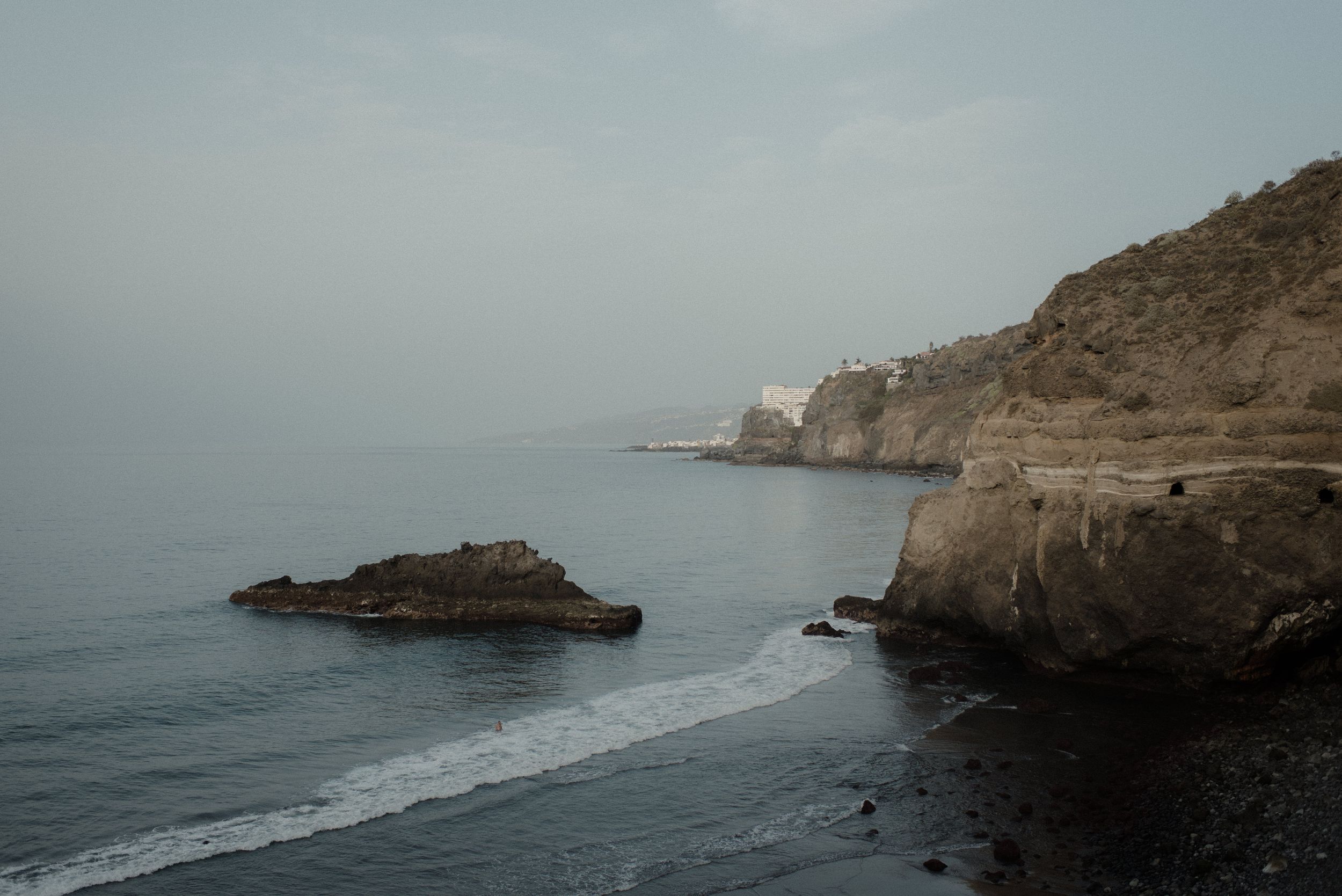 Rocky cliffs and palm trees line a dramatic coastline with waves crashing against the shore.