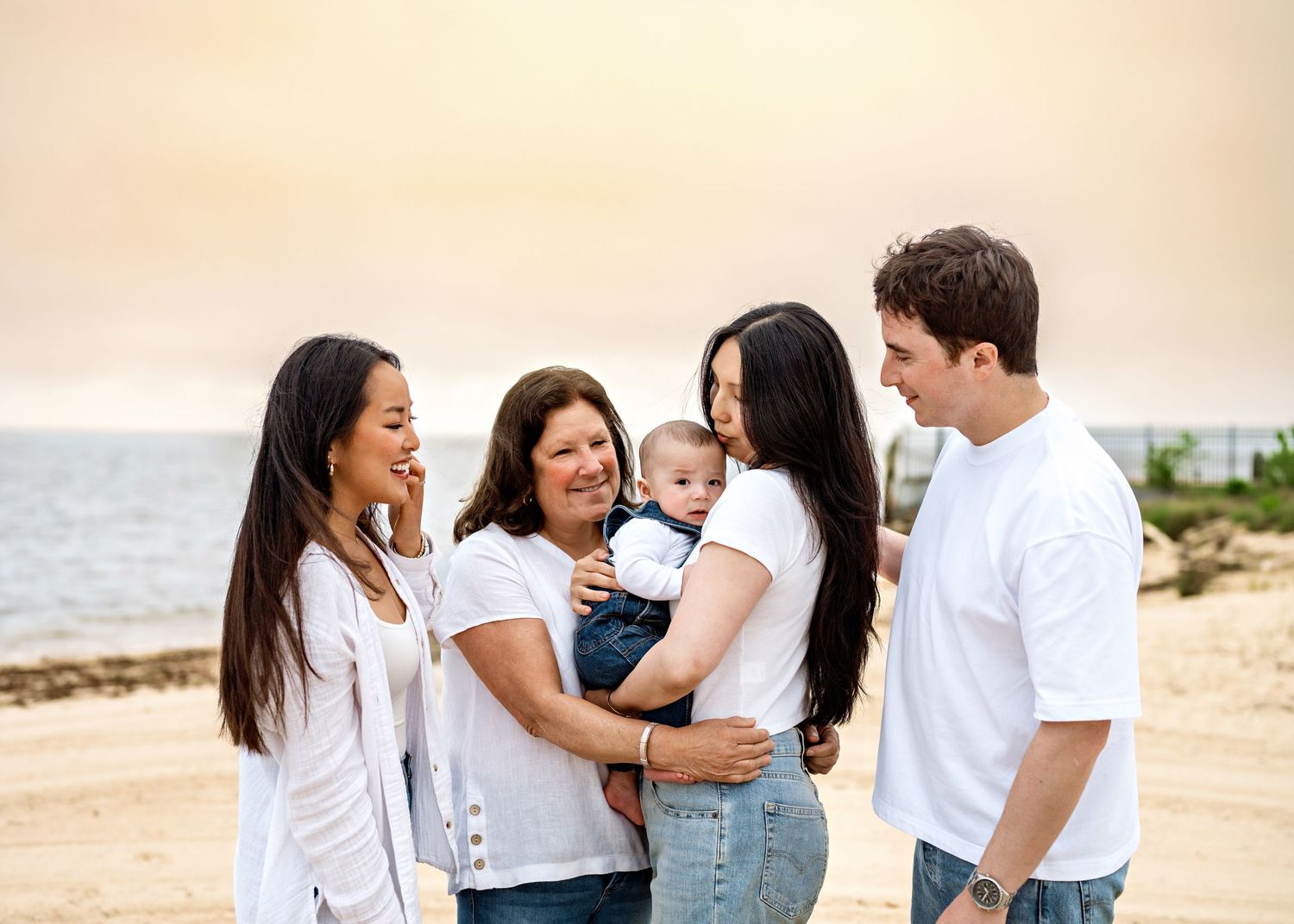 Family wearing coordinated white and denim outfits shares joyful moments together on a sunny beach.