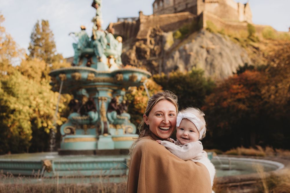 Couple enjoying a romantic autumn day in a park with golden foliage and ornate fountain in the background.