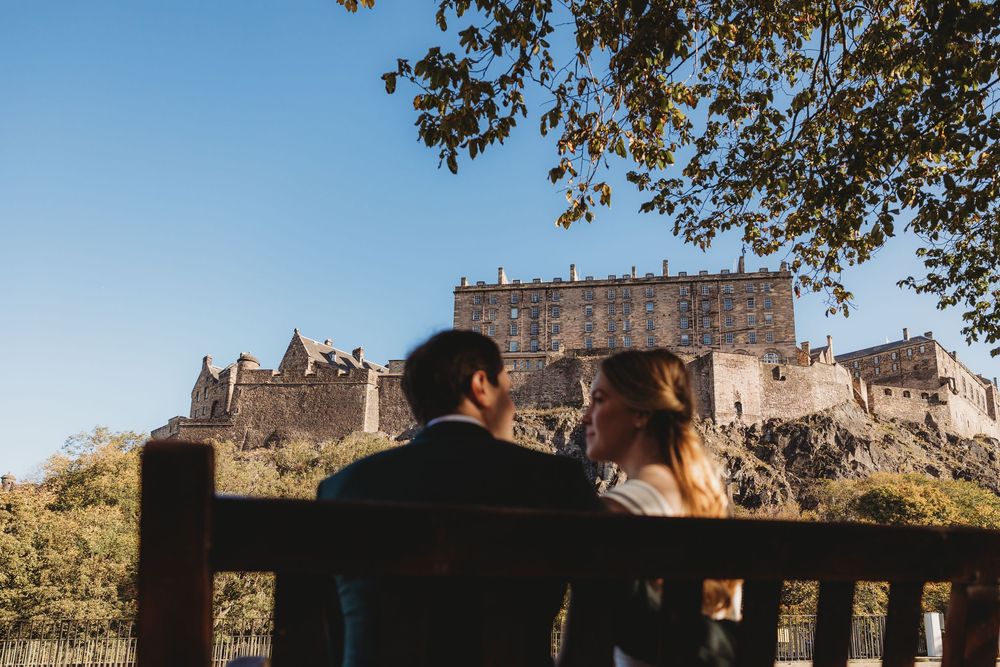 Historic stone castle walls and towers stand against a blue sky with tree branches framing the view.
