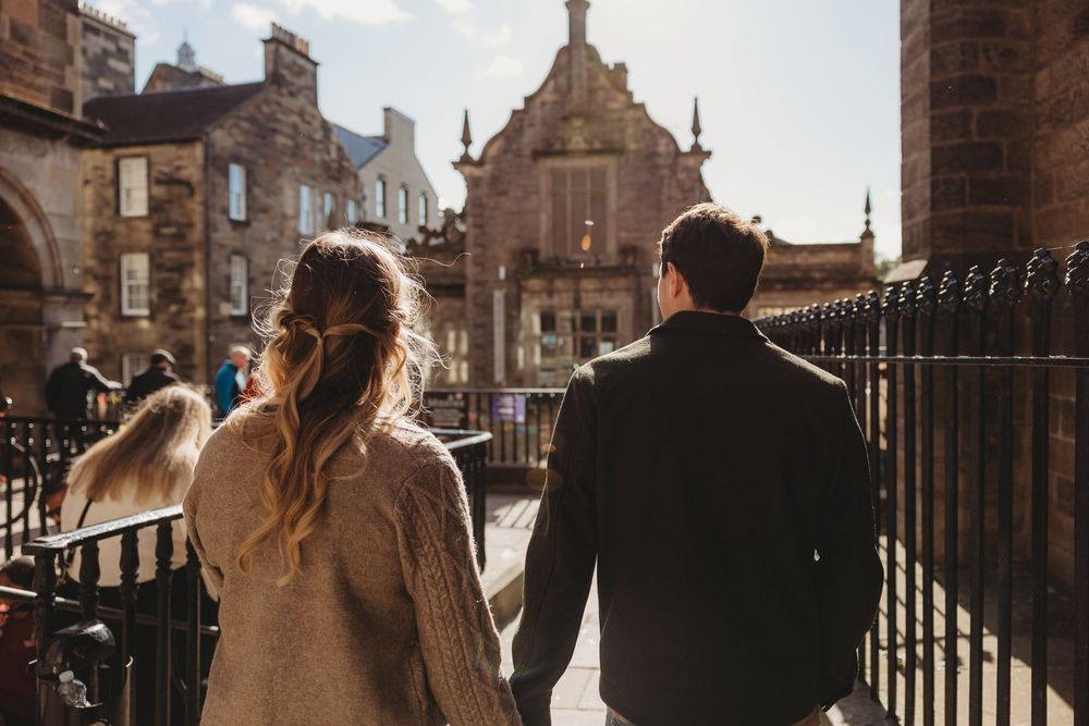 Couple walking hand in hand through historic European city streets at sunset with warm golden lighting.