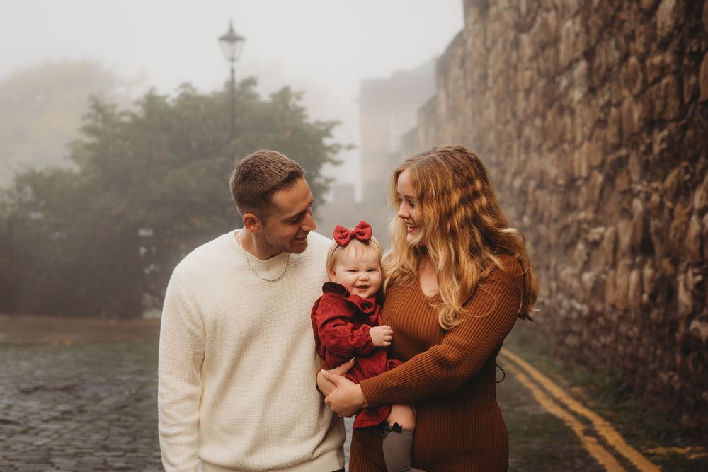 A family shares a joyful moment together on a misty road beside a stone wall.