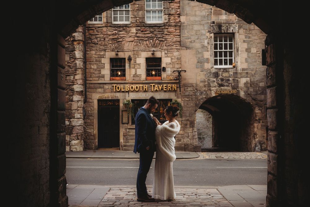 A couple in wedding attire shares an intimate moment in front of a historic stone building.
