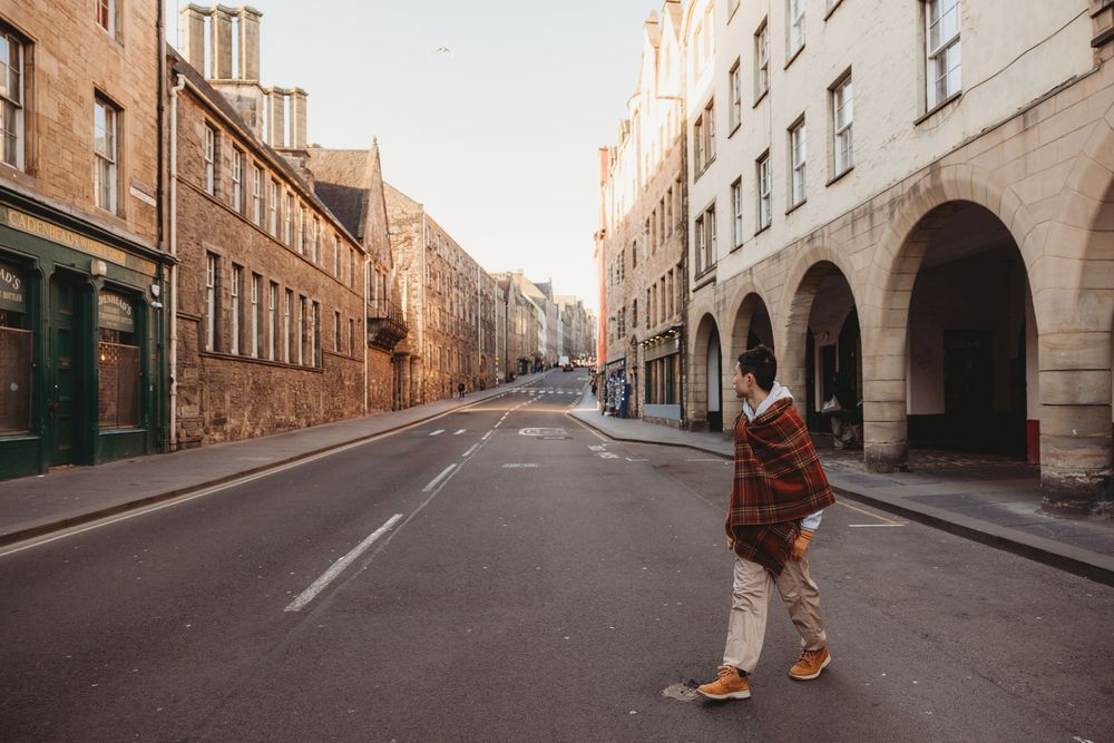 Historic stone buildings line a quiet European cobblestone street with warm sunlight casting long shadows.