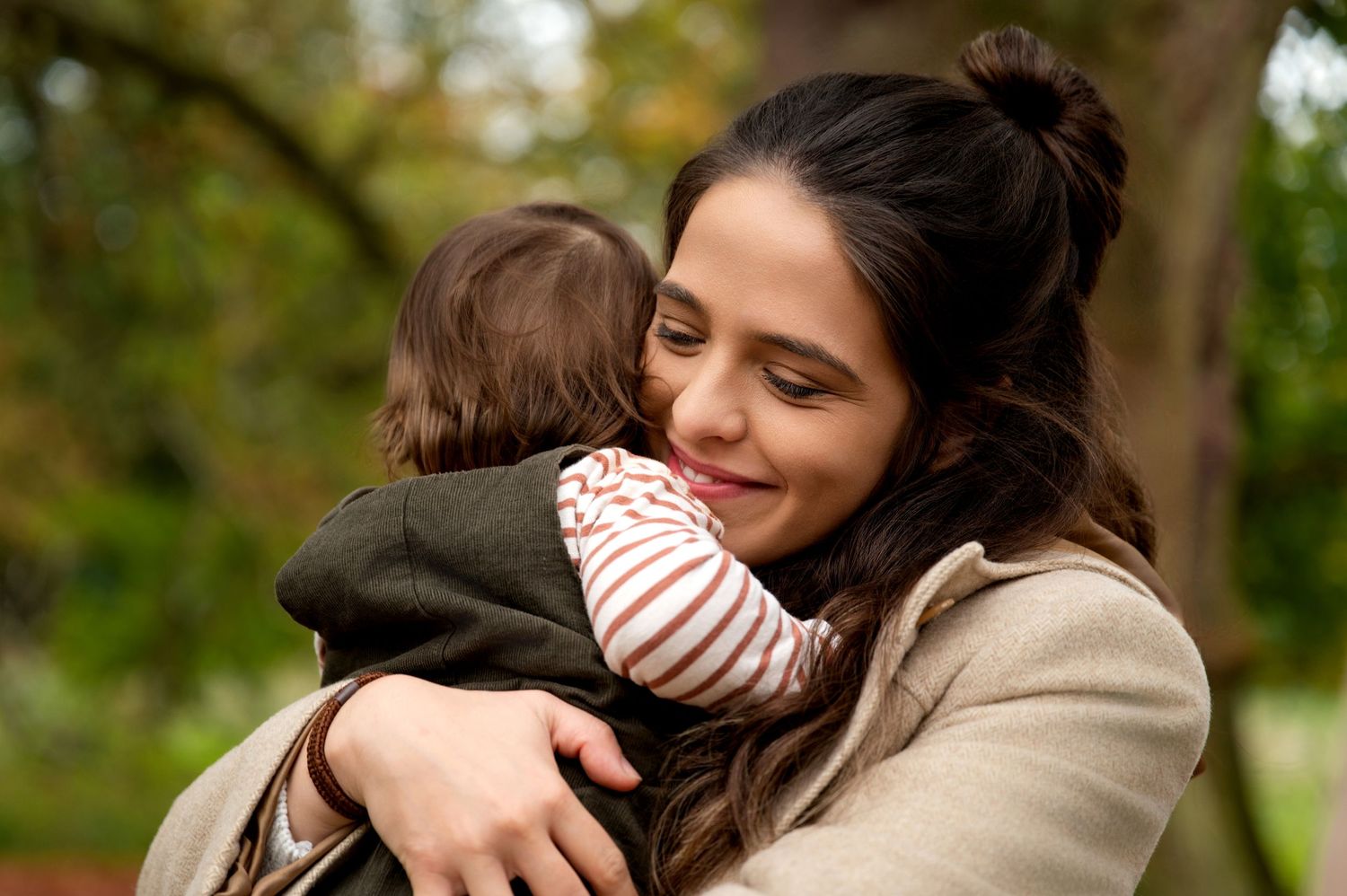 A tender moment captured as a parent embraces a small child in a striped shirt while outdoors in nature.