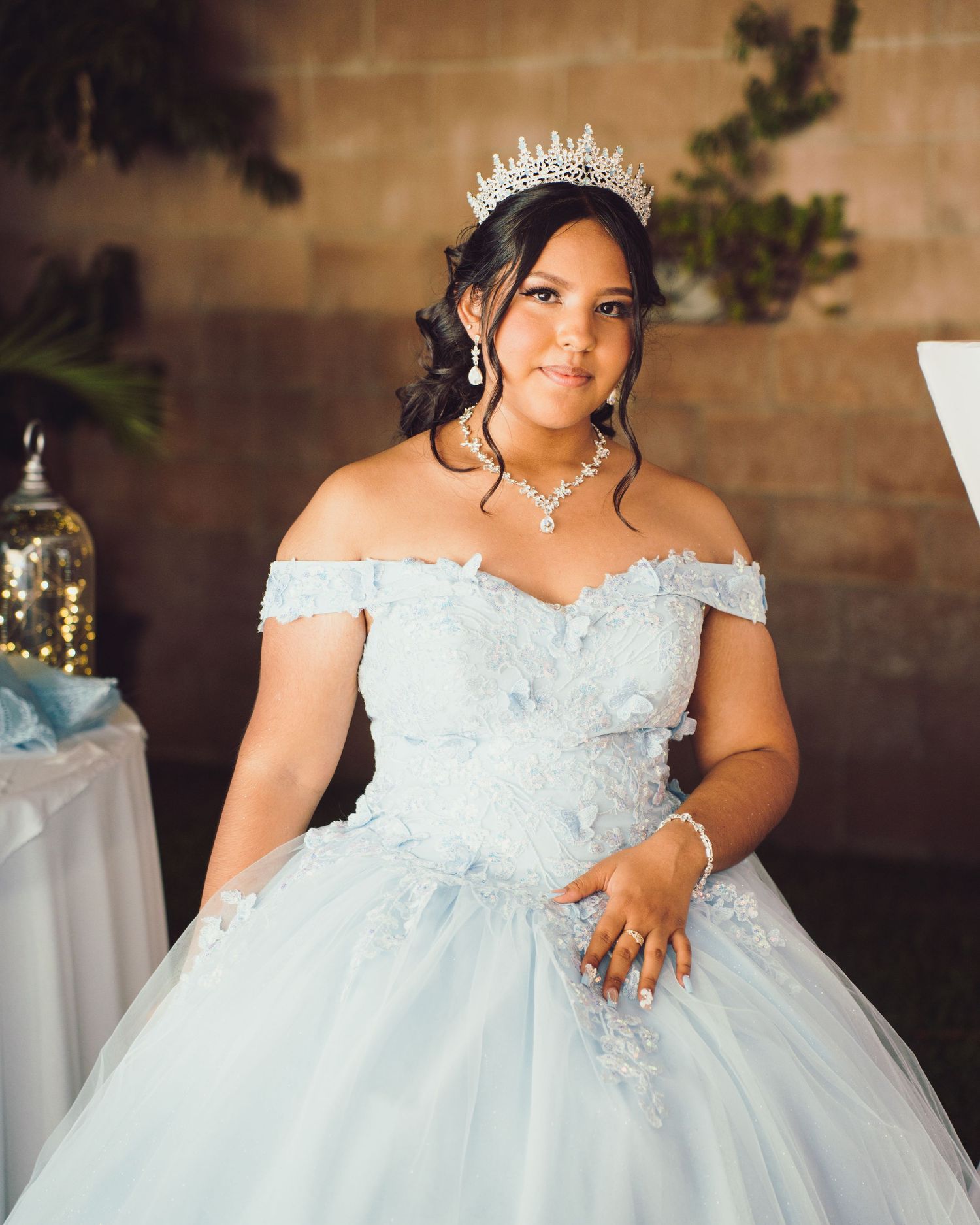 A bride in an elegant off-shoulder light blue ballgown and crystal crown poses during her special celebration.