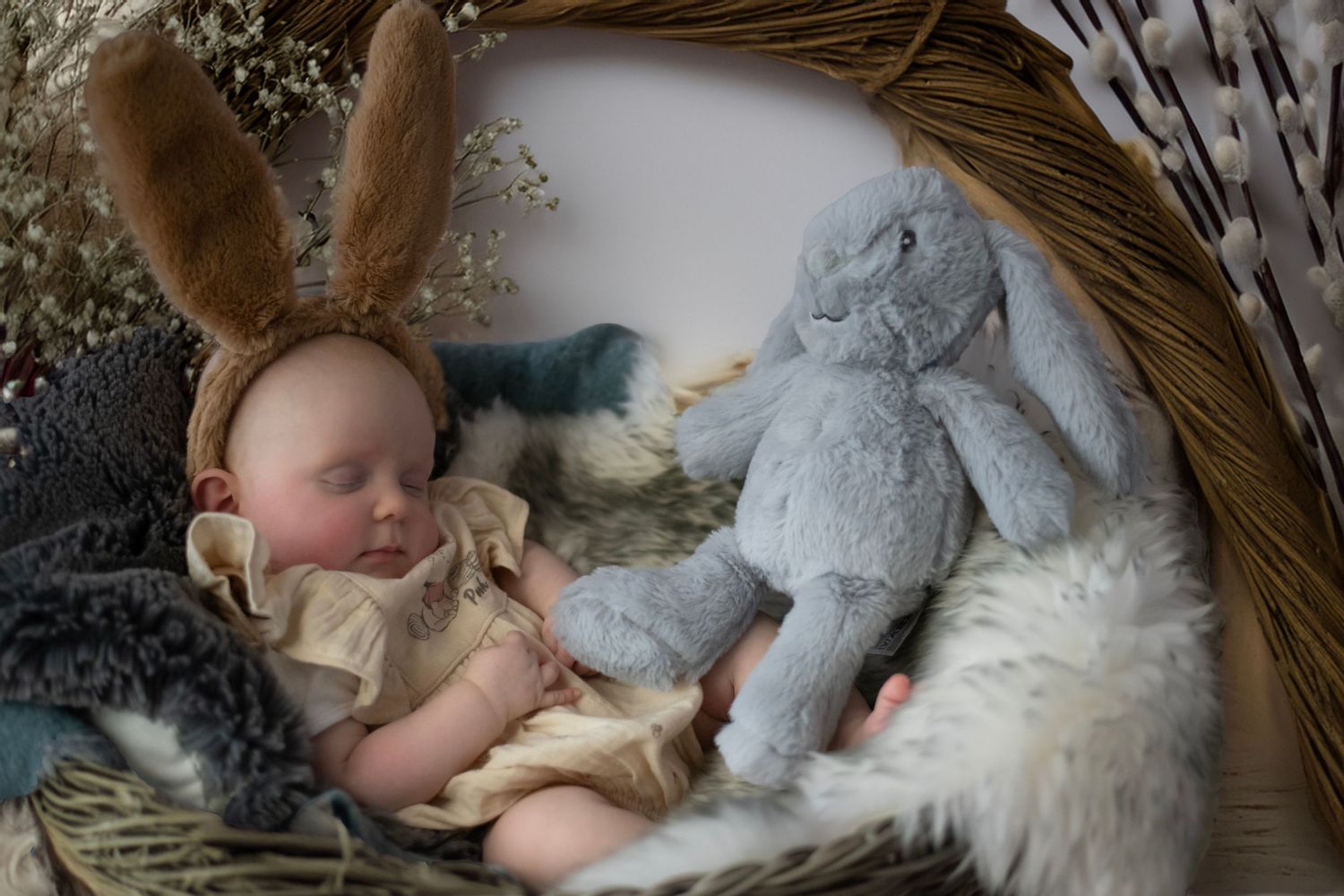 A sleeping baby lies peacefully next to a fluffy white dog in a cozy wicker basket.