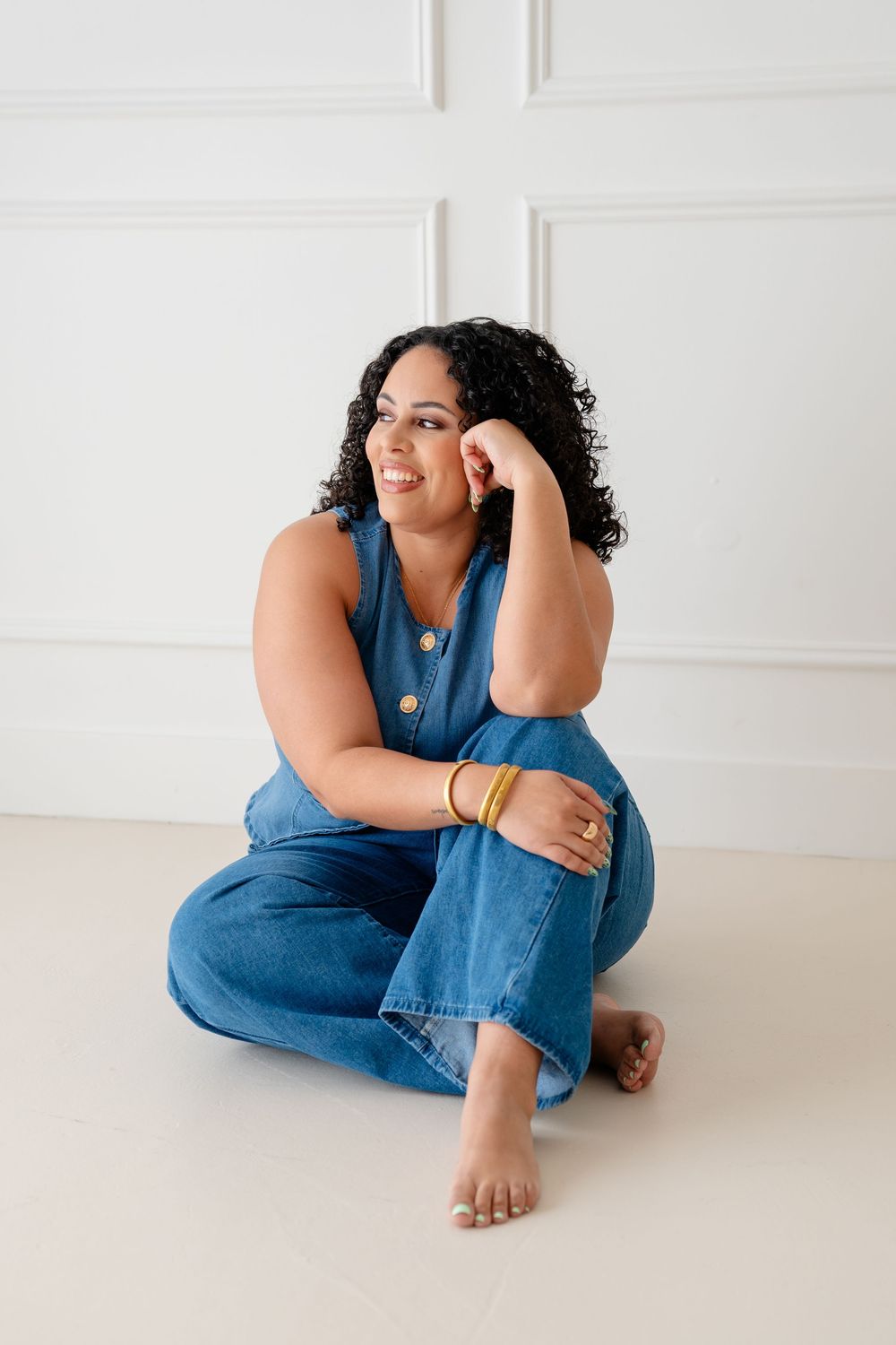 A person in denim overalls sits on a white floor in a minimalist setting, shown in multiple artistic poses.