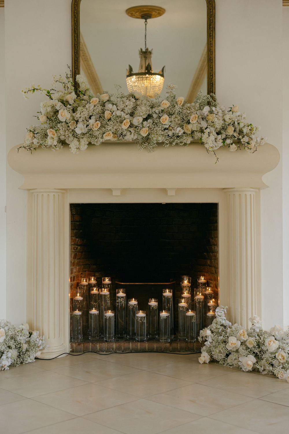 White floral arrangements adorn an elegant fireplace mantel in a bright, minimalist wedding venue setting.