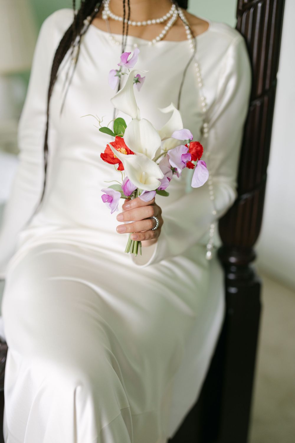 A person in a white long-sleeved dress holds delicate pink and white flowers against a light background.